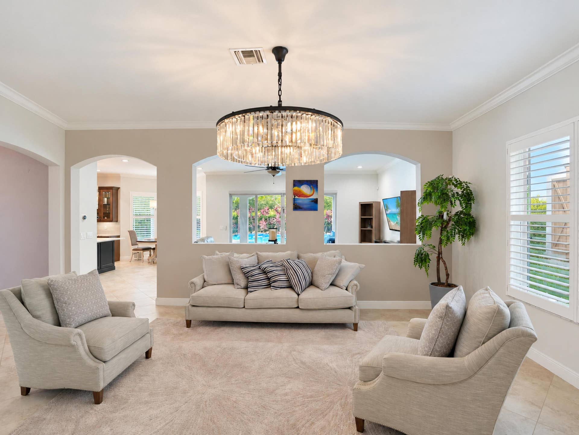 8601 Waterside Court, Parkland, FL 33076 Living space featuring a large-scale drum chandelier with crystal accents, dual arched wall cutouts, crown molding, and plantation shutters