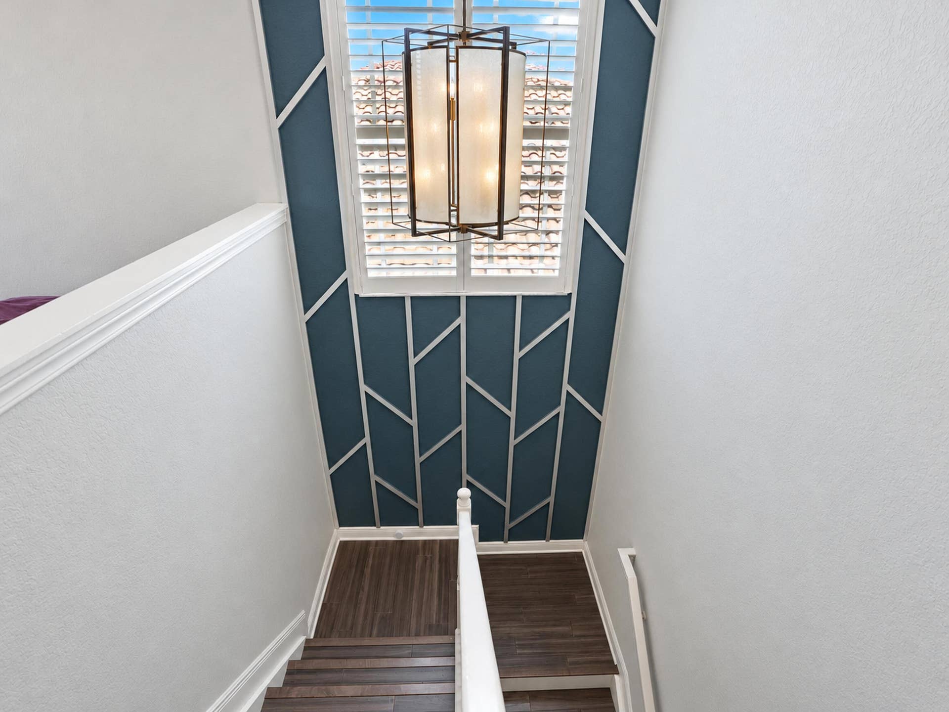 8601 Waterside Court, Parkland, FL 33076 Staircase featuring wood-finish treads, geometric accent wall molding, tiered metal pendant lighting, and plantation shutters