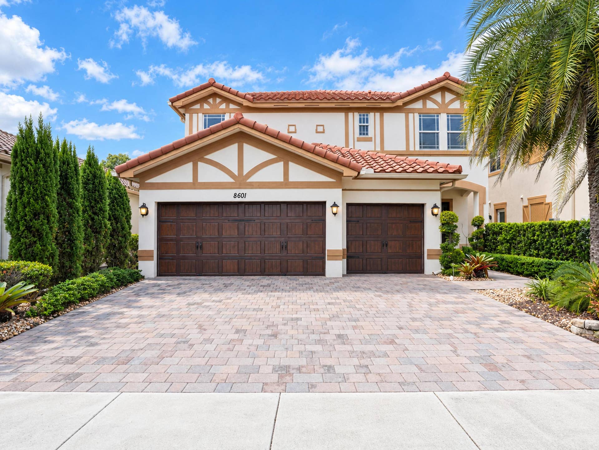 8601 Waterside Court, Parkland, FL 33076 Two-story exterior featuring a clay tile roof, stucco facade with decorative timbering, paver driveway, and a three-car garage with wood-finish doors