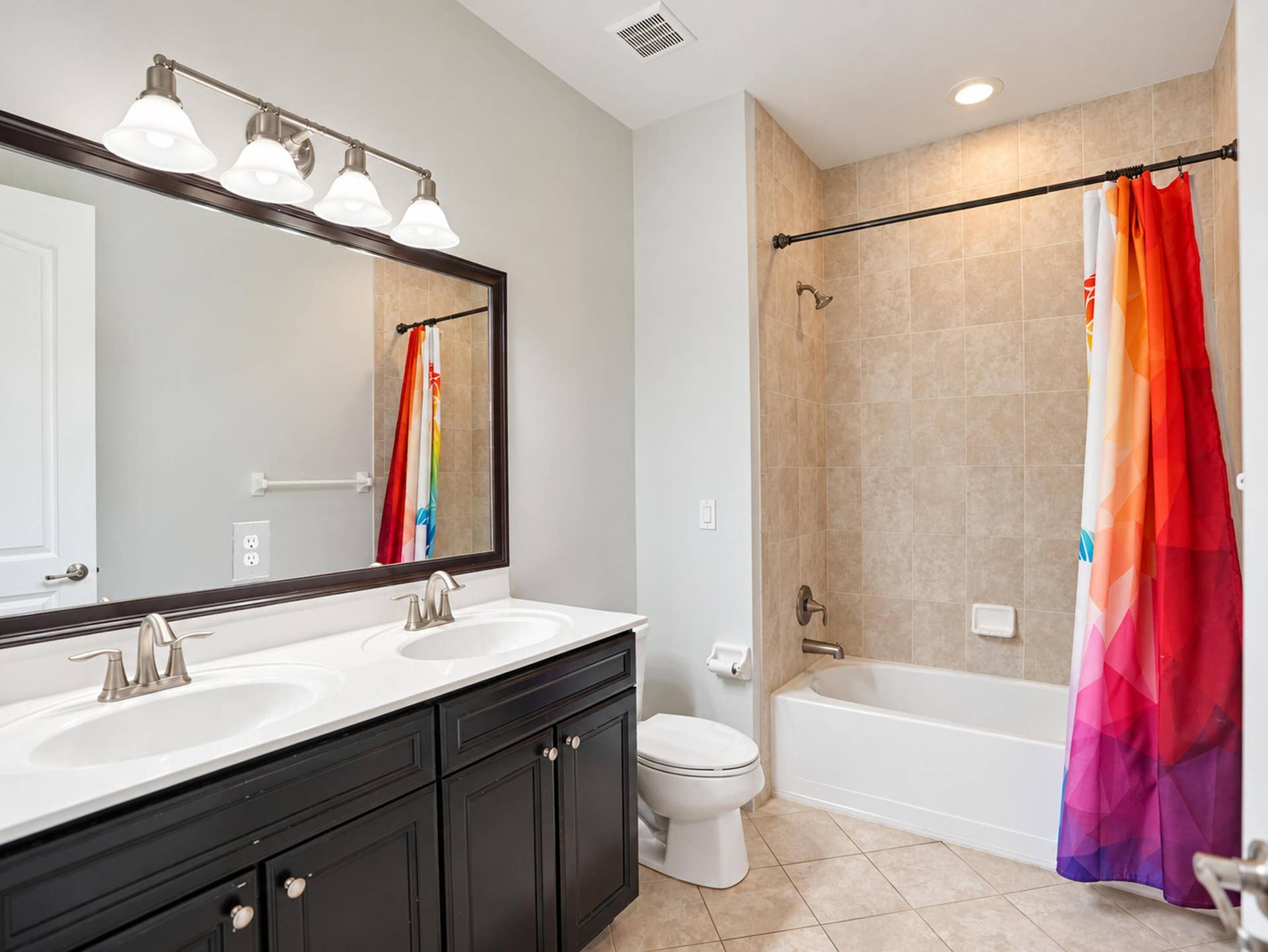 8601 Waterside Court, Parkland, FL 33076 Double vanity featuring dark cabinetry, solid surface countertops with dual integrated sinks, four-light vanity fixture, and tiled tub and shower combination
