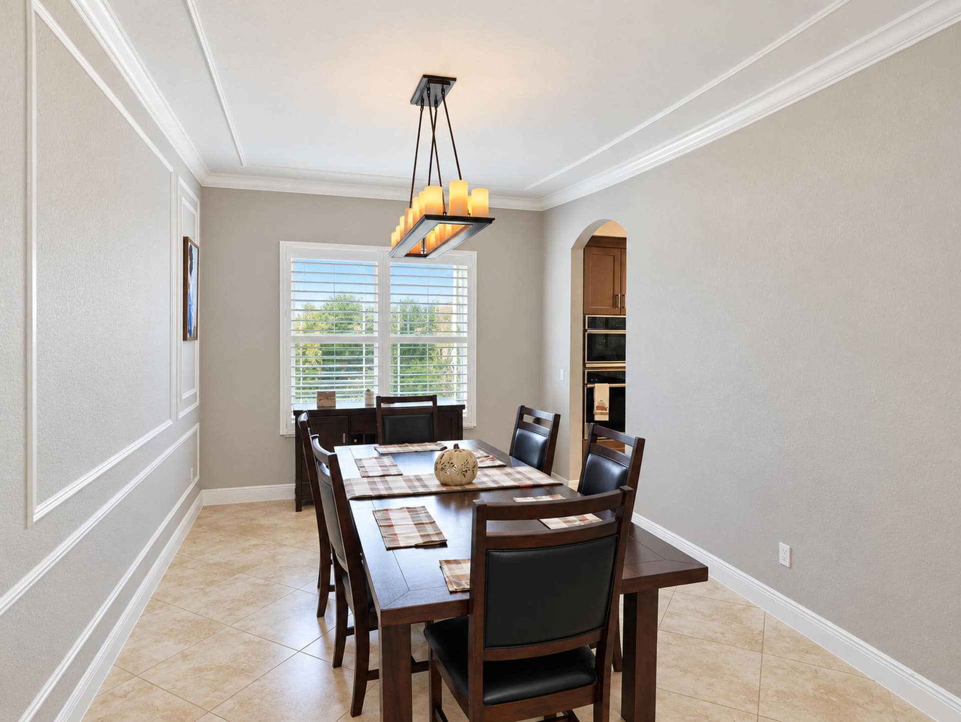 8601 Waterside Court, Parkland, FL 33076 Dining area featuring crown molding, wainscot wall paneling, tile flooring, and a multi-light chandelier