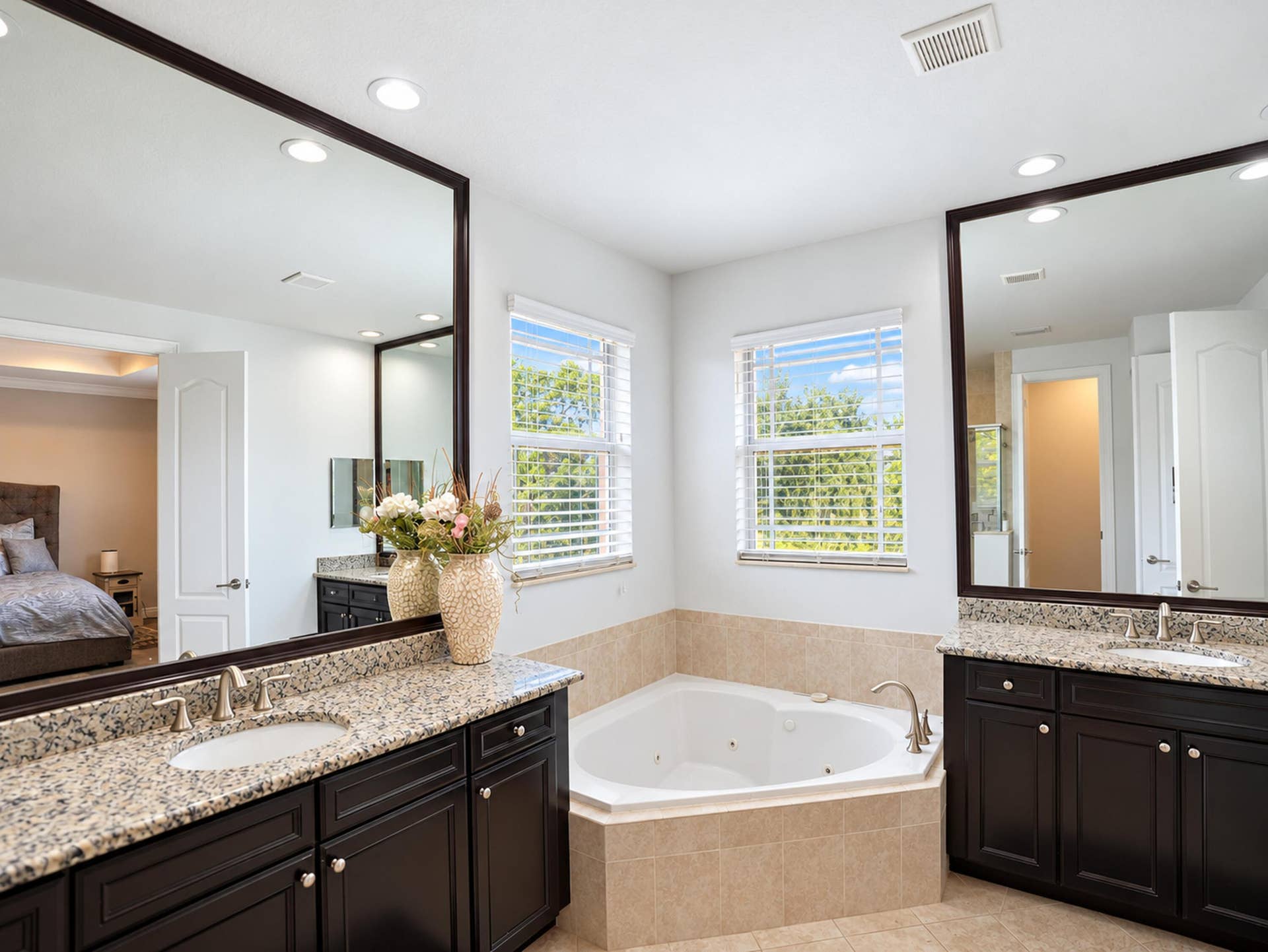8601 Waterside Court, Parkland, FL 33076 Dual vanities with dark-finish cabinetry, stone-style countertops, integrated undermount sinks, and large-format framed mirrors, featuring a soaking jetted tub set in a tile-surround platform
