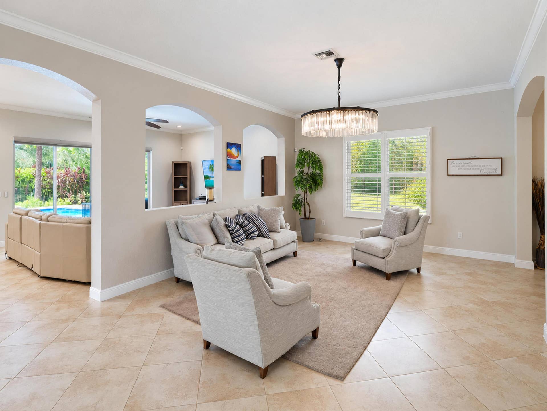 8601 Waterside Court, Parkland, FL 33076 Neutral-toned interior featuring large-format ceramic tile flooring, architectural arched cutouts, crown molding, and a tiered crystal drum chandelier