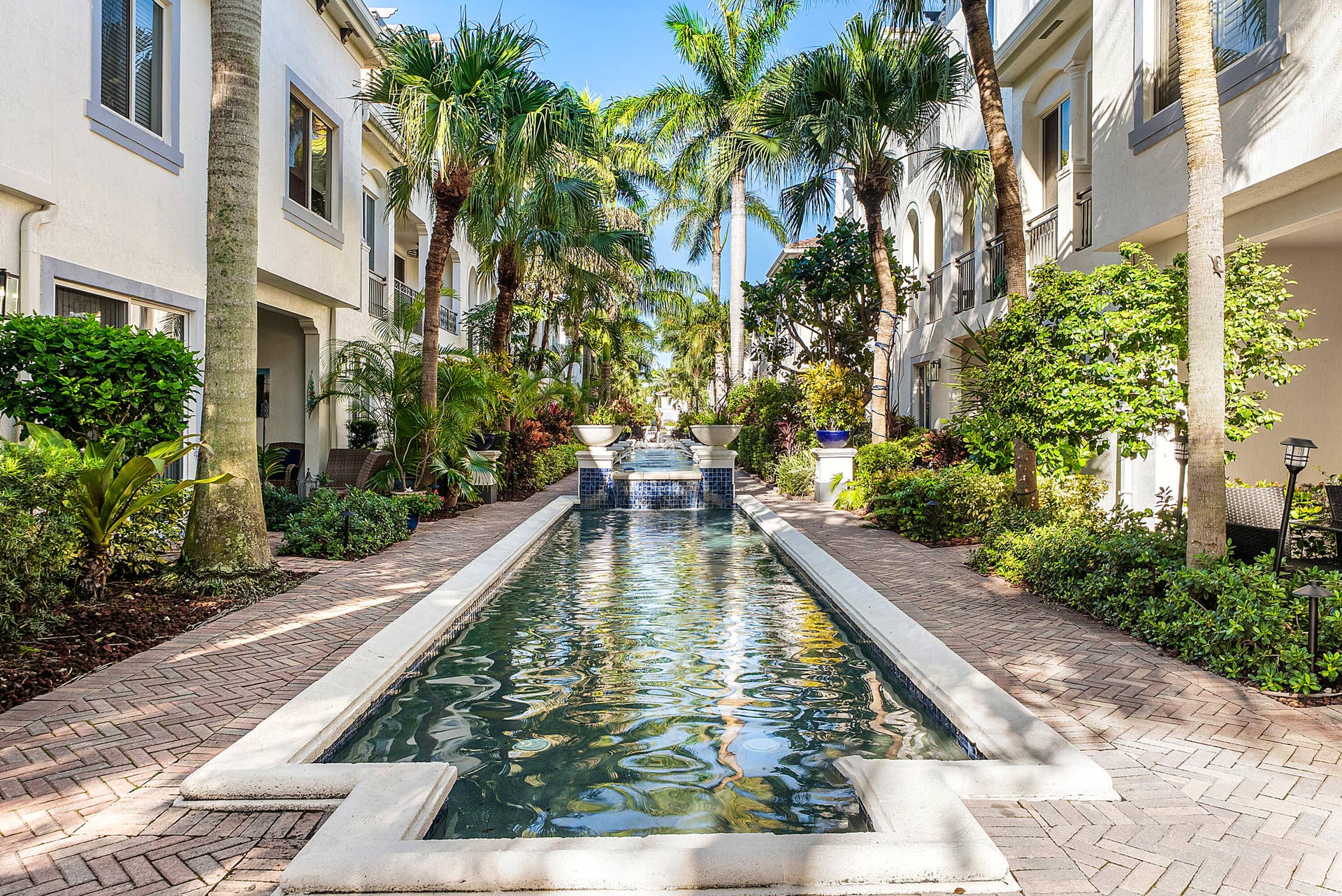 Elongated water feature with tiered fountain, surrounded by mature palm trees and lush landscaping