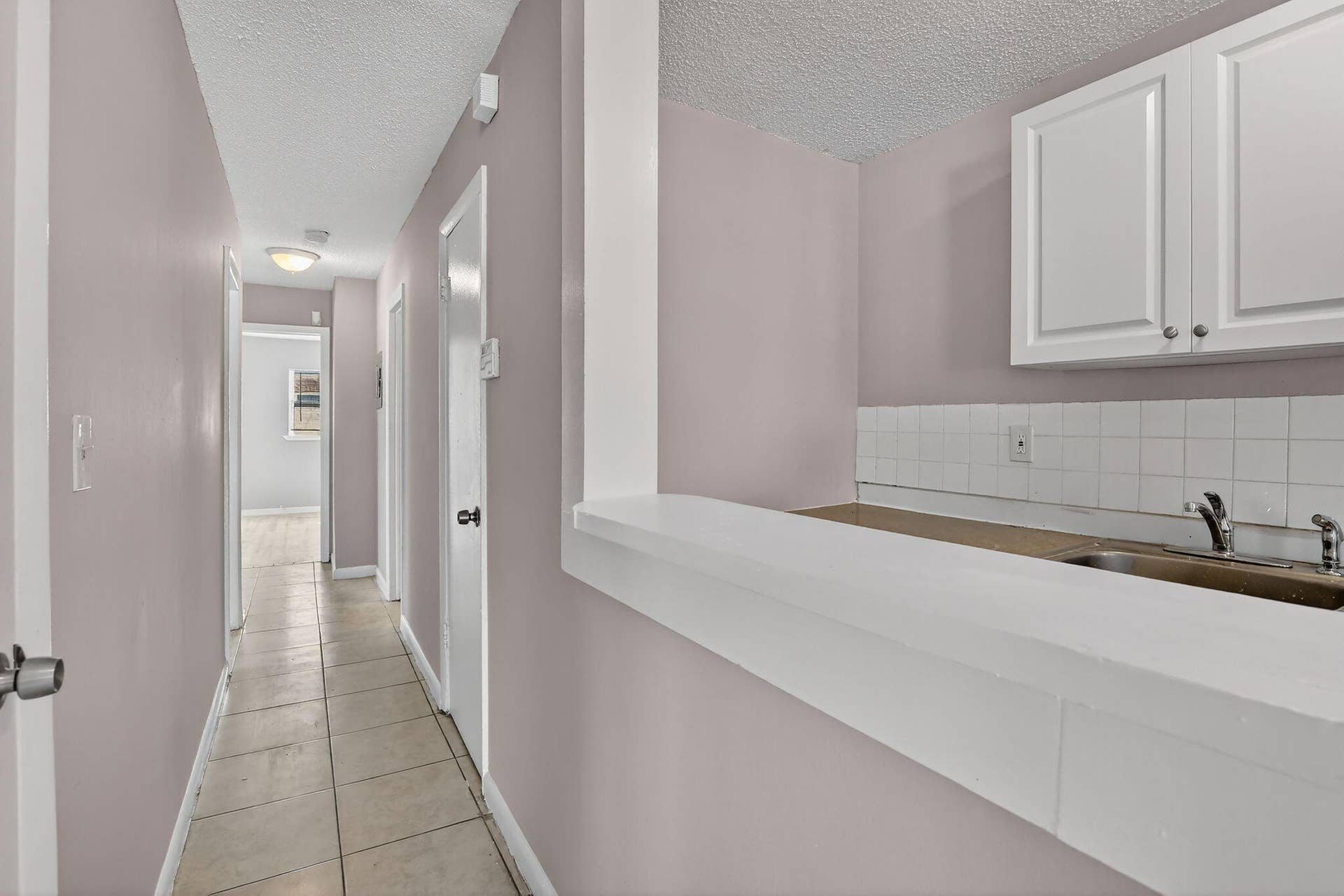 Hallway featuring tile flooring, white shaker-style cabinetry, and a pass-through counter with a tiled backsplash