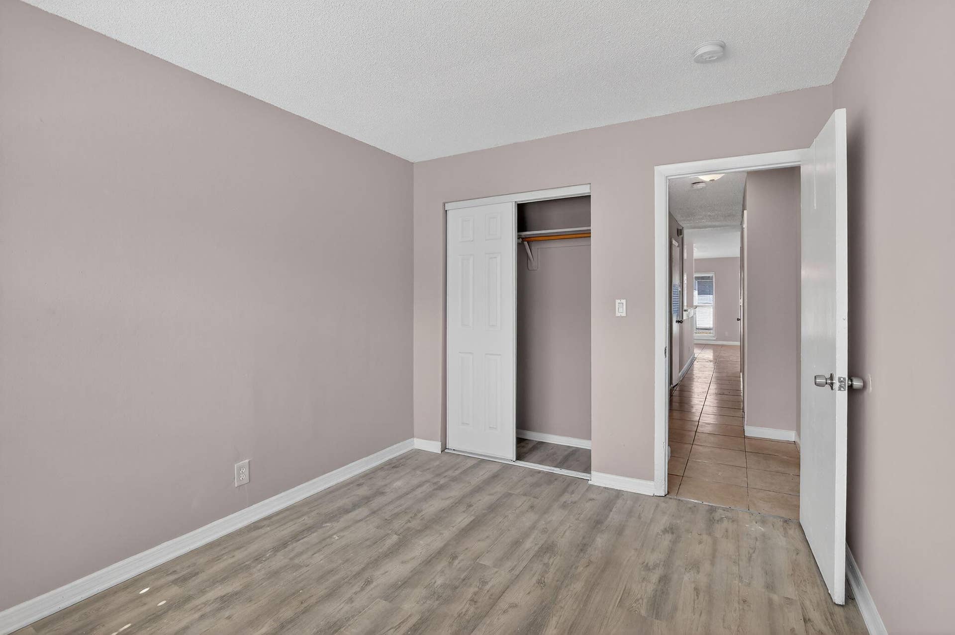 Room featuring wood-finish flooring, a sliding-door closet with a built-in rod, and a standard swinging door with a metallic knob