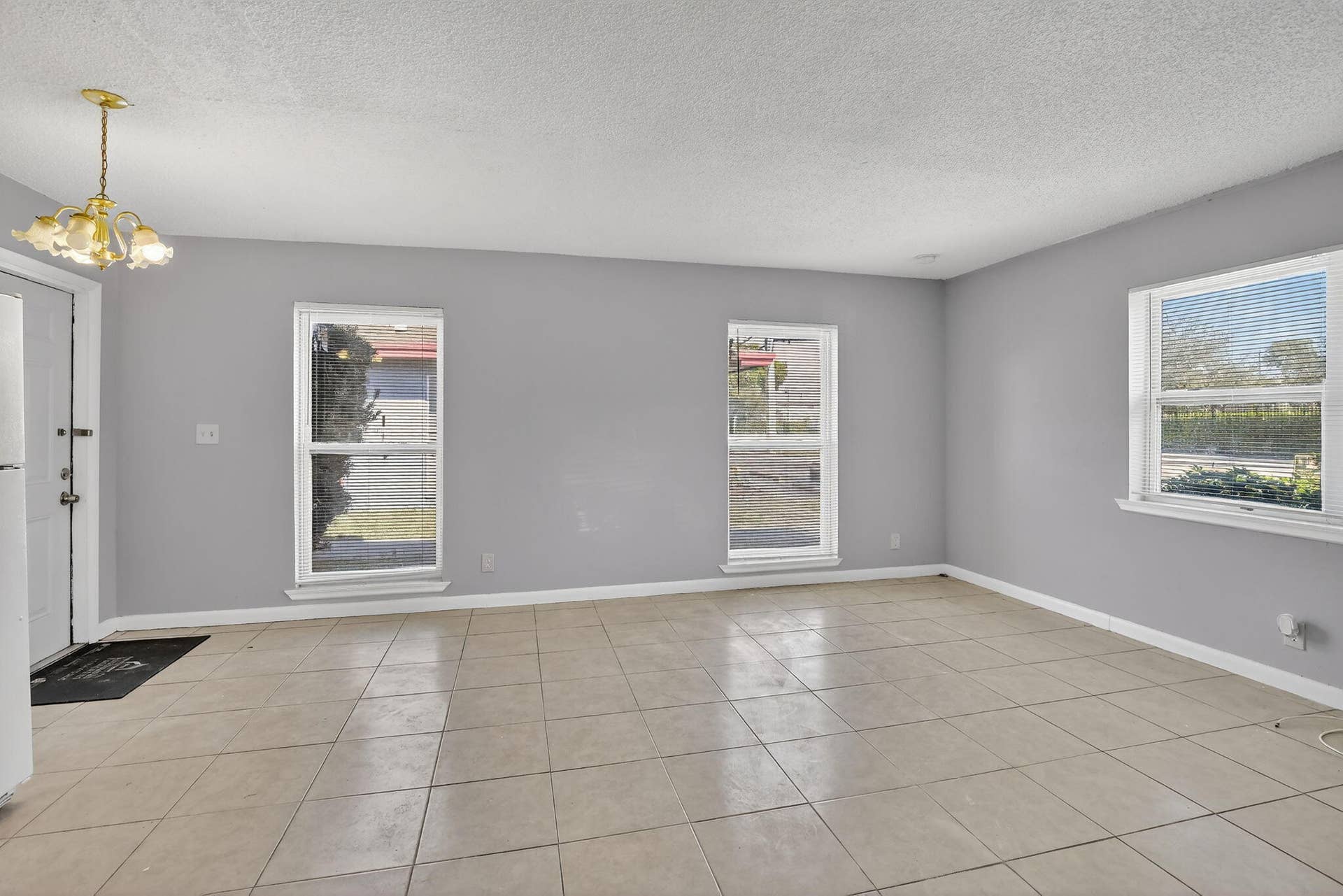 Neutral-toned interior space featuring light-colored ceramic tile flooring, three large windows, and a multi-arm metallic light fixture