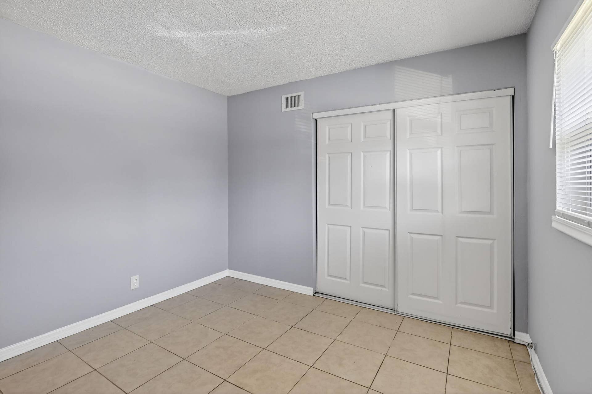 Neutral wall finish, large-format tile flooring, and a double-door sliding closet