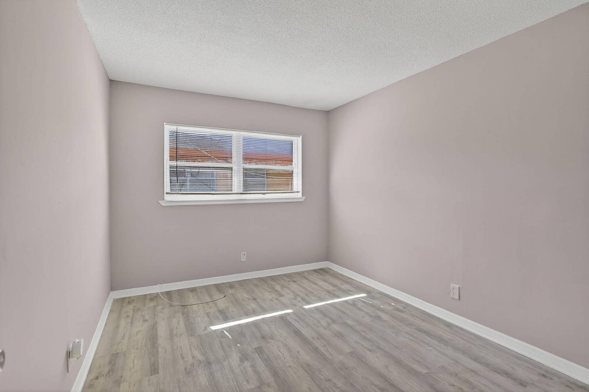 Room featuring neutral-toned walls, wood-finish flooring, and a large picture window with integrated blinds