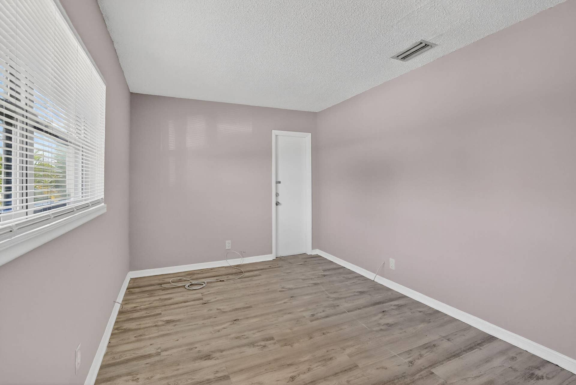 Neutral-toned interior room featuring wood-finish flooring, textured ceiling, and large horizontal window with fitted blinds