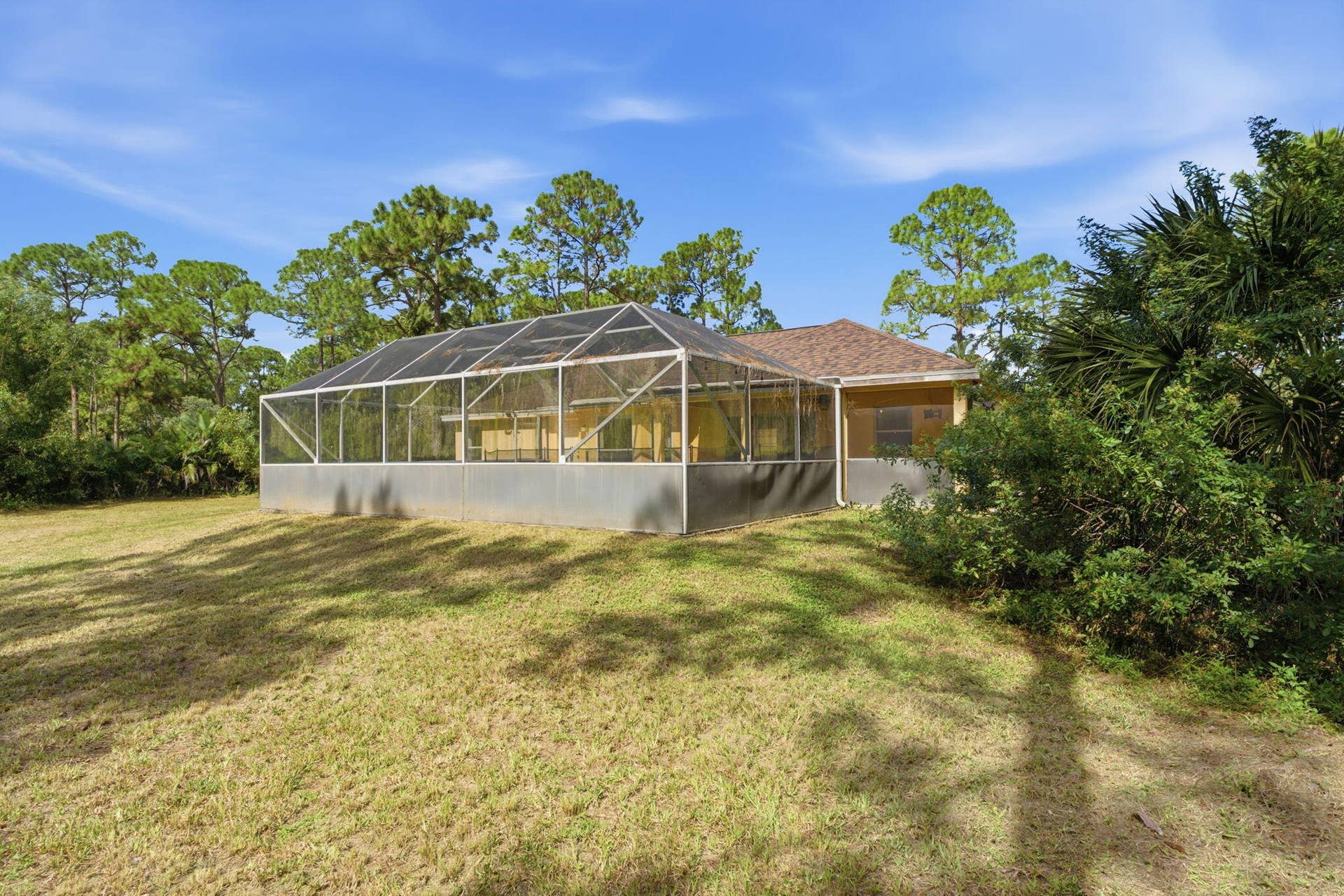 Screened-in rear porch featuring an aluminum frame, shingle roofing, and expansive grounds with mature trees