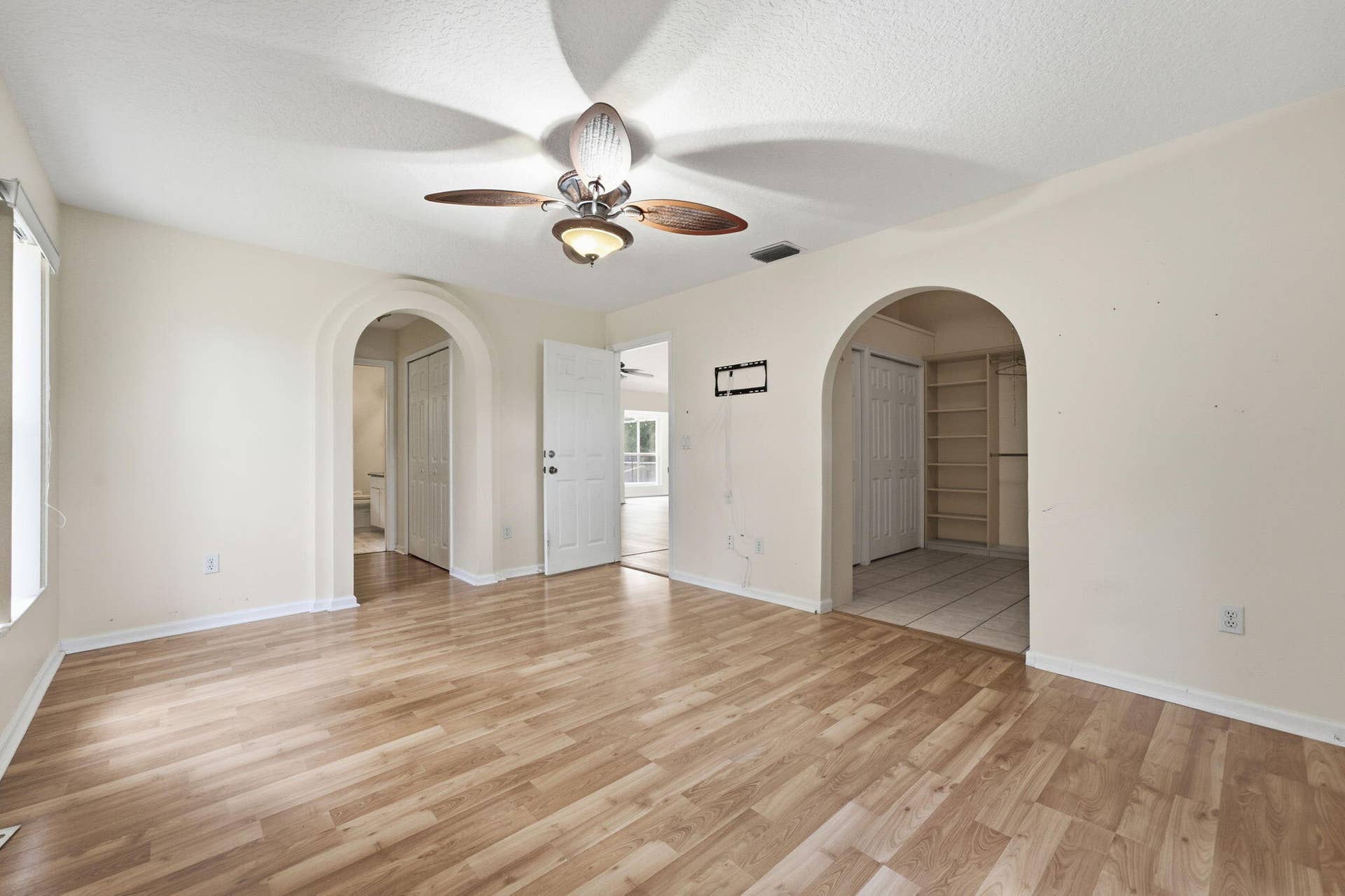 Interior space featuring wood-finish flooring, two arched entryways, ceiling fan with integrated lighting, and built-in shelving