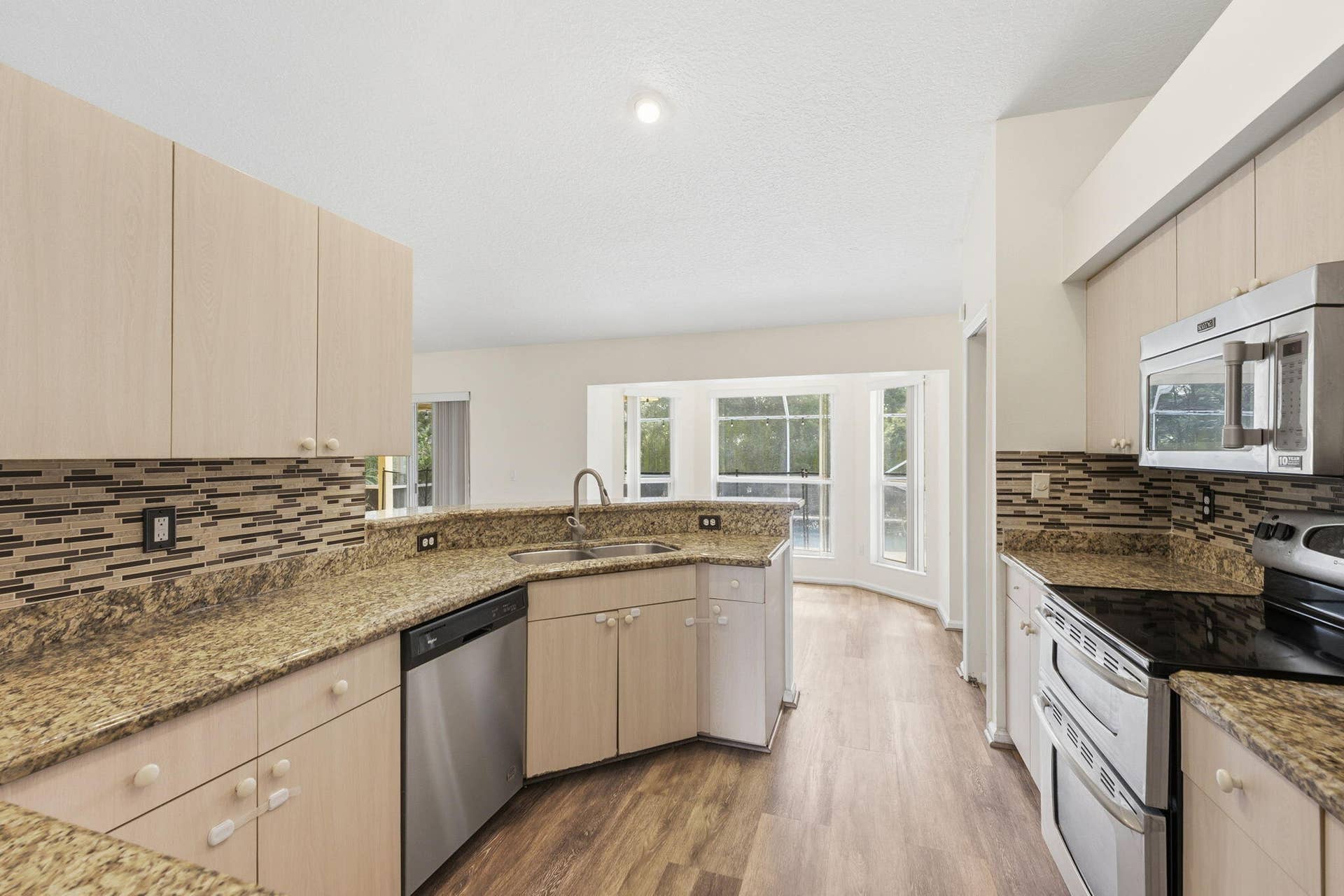 Kitchen featuring light-finish cabinetry, stone-texture countertops, mosaic tile backsplash, wood-finish flooring, and stainless steel appliances