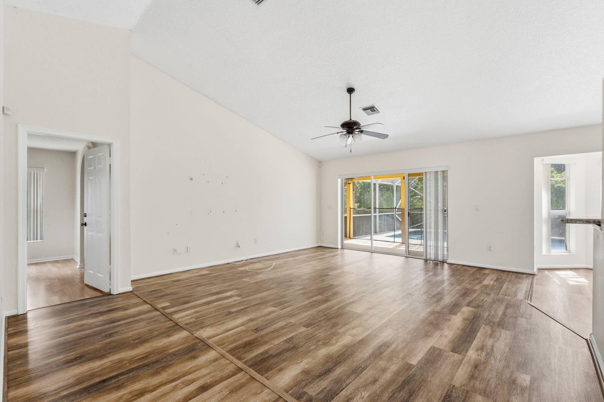 Vaulted ceilings, wood-finish flooring, central ceiling fan, and sliding glass doors providing outdoor access