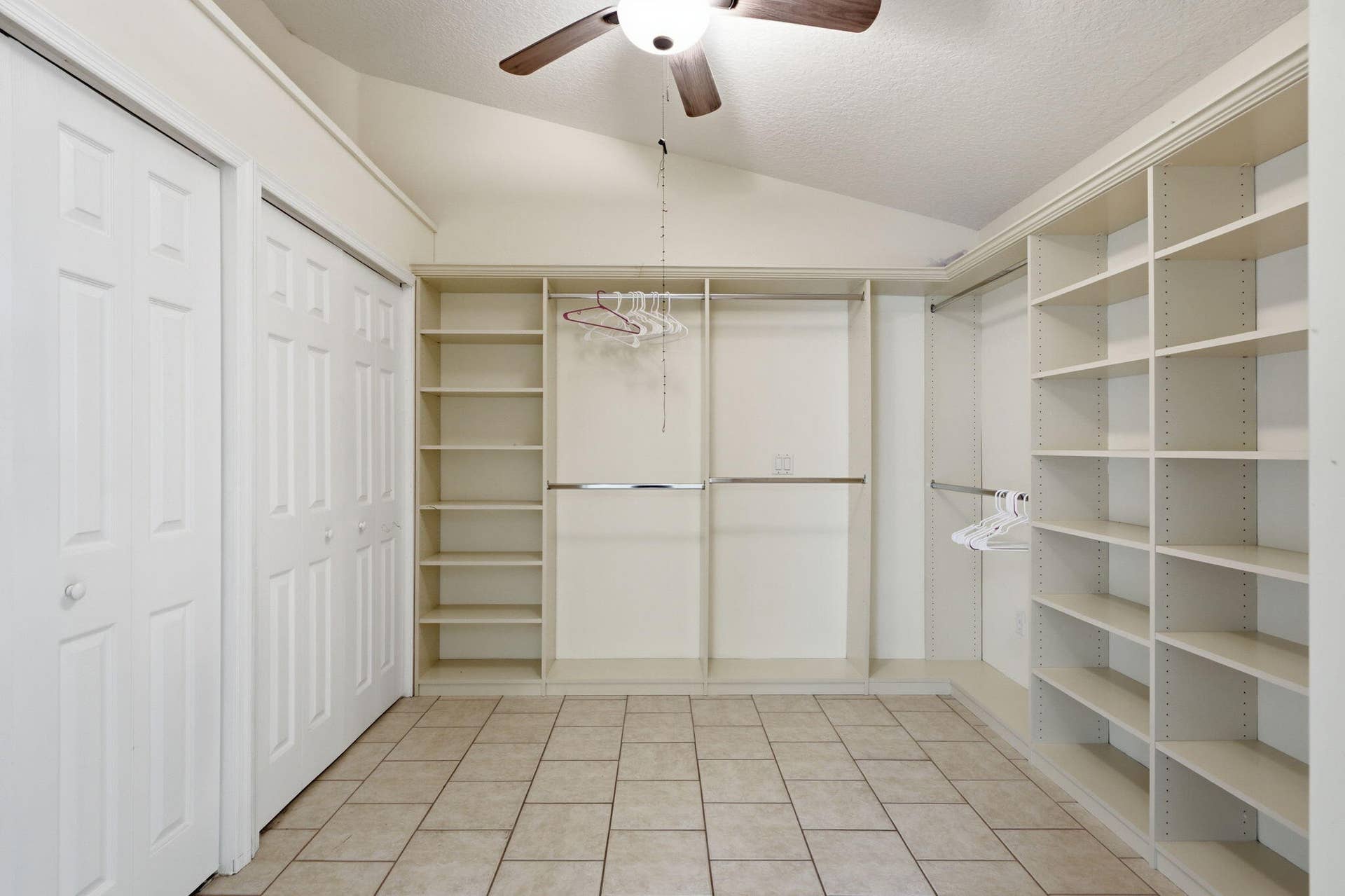 Walk-in closet featuring vaulted ceilings, custom built-in shelving, dual hanging rods, tile flooring, and overhead lighting with an integrated ceiling fan