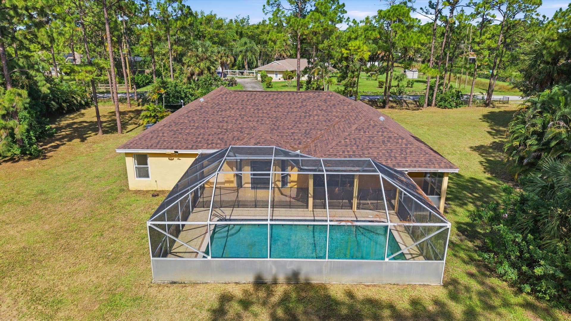 Aerial perspective of a detached residence featuring a screened-in swimming pool, a concrete pool deck, and a multi-sloped roofline situated on a lot with mature perimeter trees