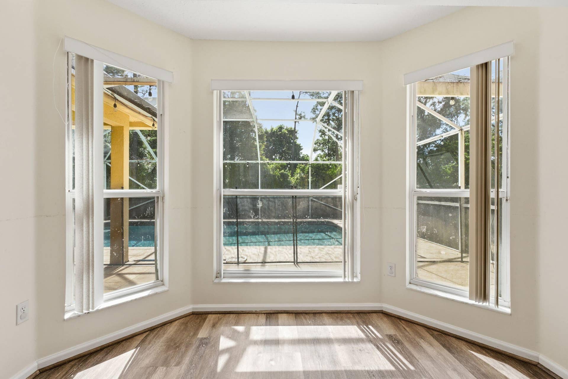 Bay window featuring wood-finish flooring and vertical blinds, showcasing an enclosed pool area