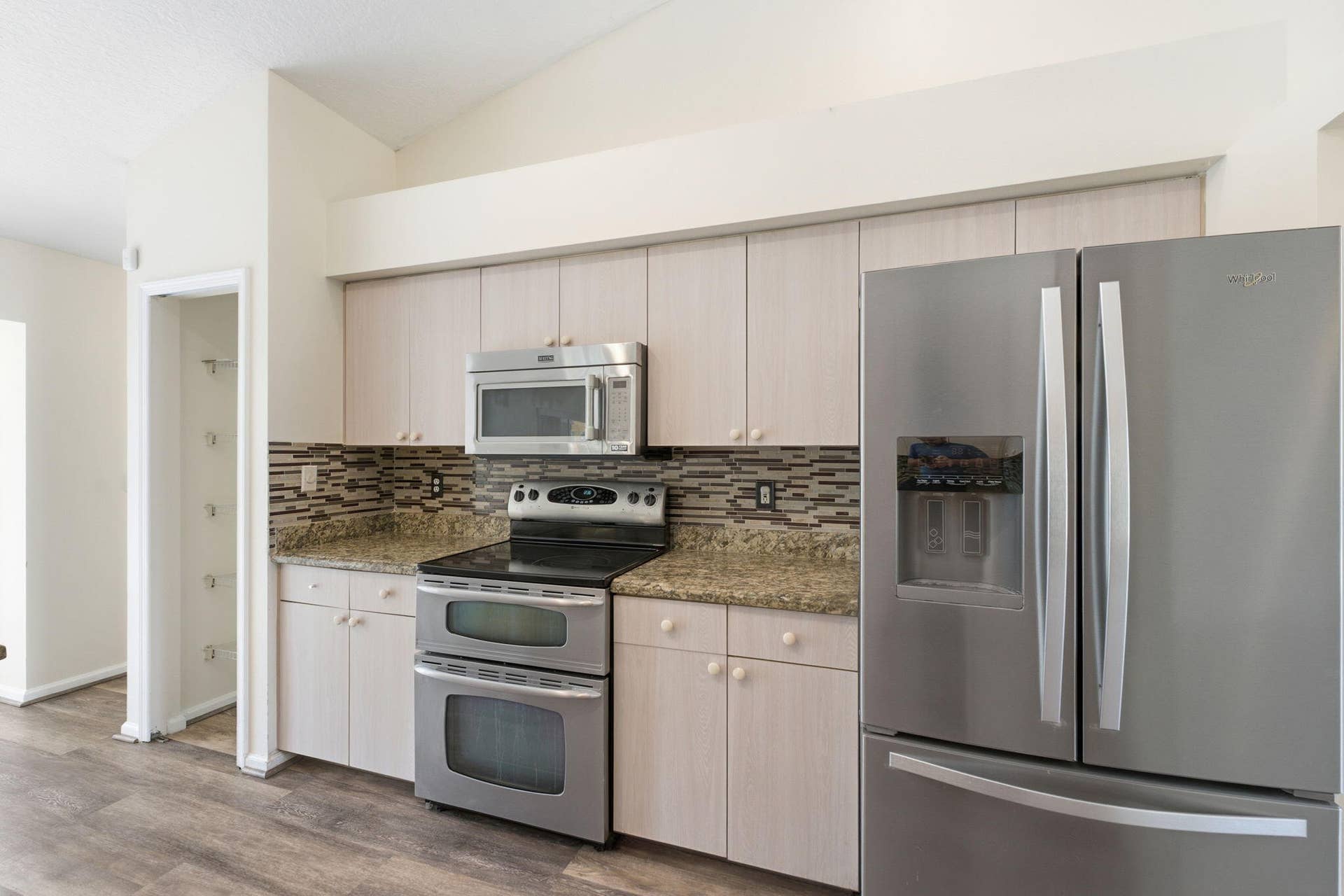 Kitchen featuring light-finish cabinetry, stone-texture countertops, multi-tonal backsplash tile, and stainless steel appliances including a double-oven range and French-door refrigerator