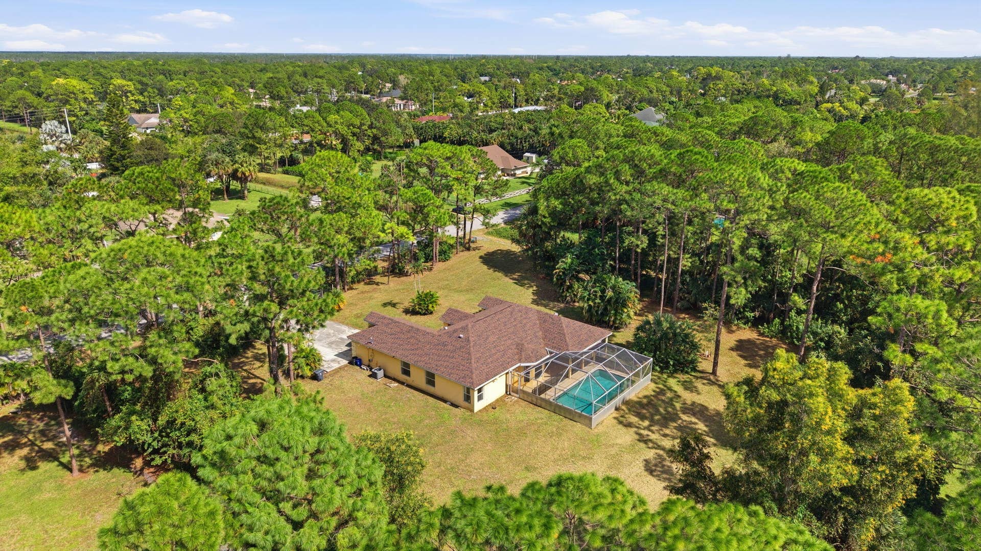 Aerial view of a sprawling property featuring a multi-gabled roofline, an enclosed pool, and extensive grounds surrounded by mature trees