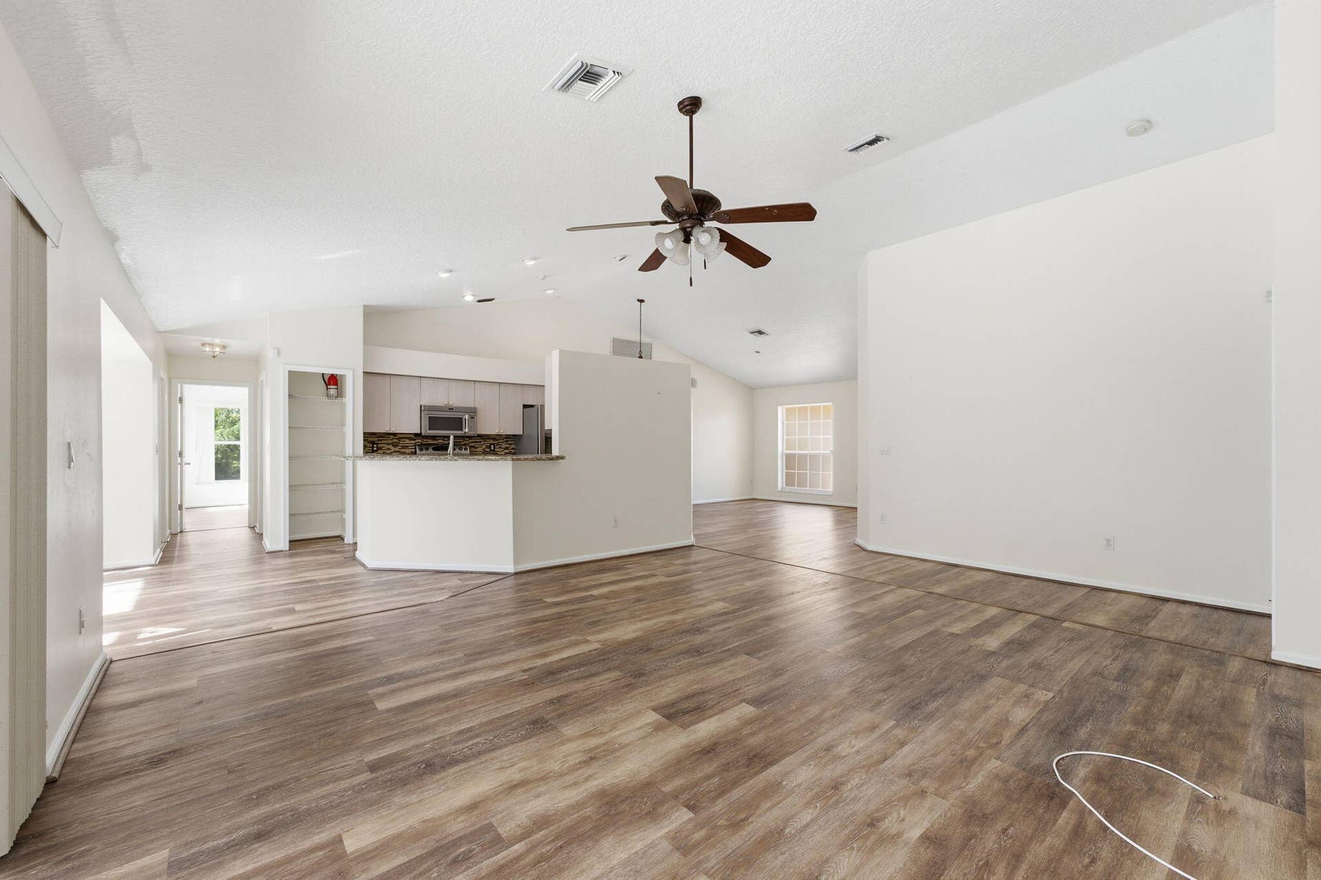 Open-concept floor plan featuring vaulted ceilings, wood-finish flooring, a kitchen breakfast bar, and a ceiling fan with integrated lighting