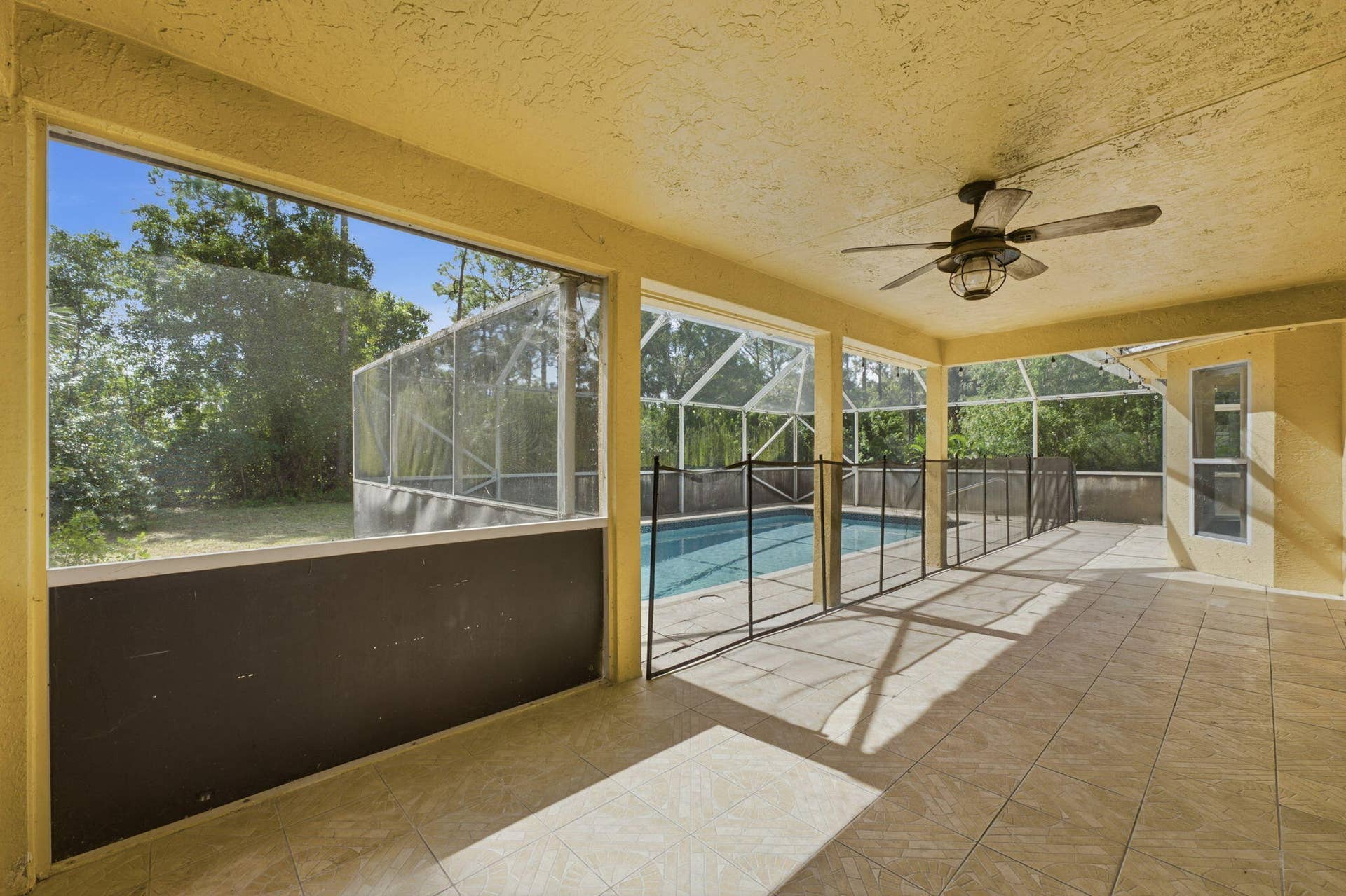 Screened-in lanai featuring tile flooring, a mounted ceiling fan, and a swimming pool enclosed by a metal safety fence