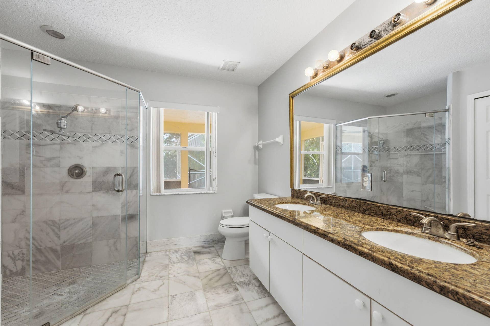 Double vanity featuring a stone countertop, under-mount sinks, a full-width mirror, and a walk-in glass-enclosed shower with stone-style wall tile