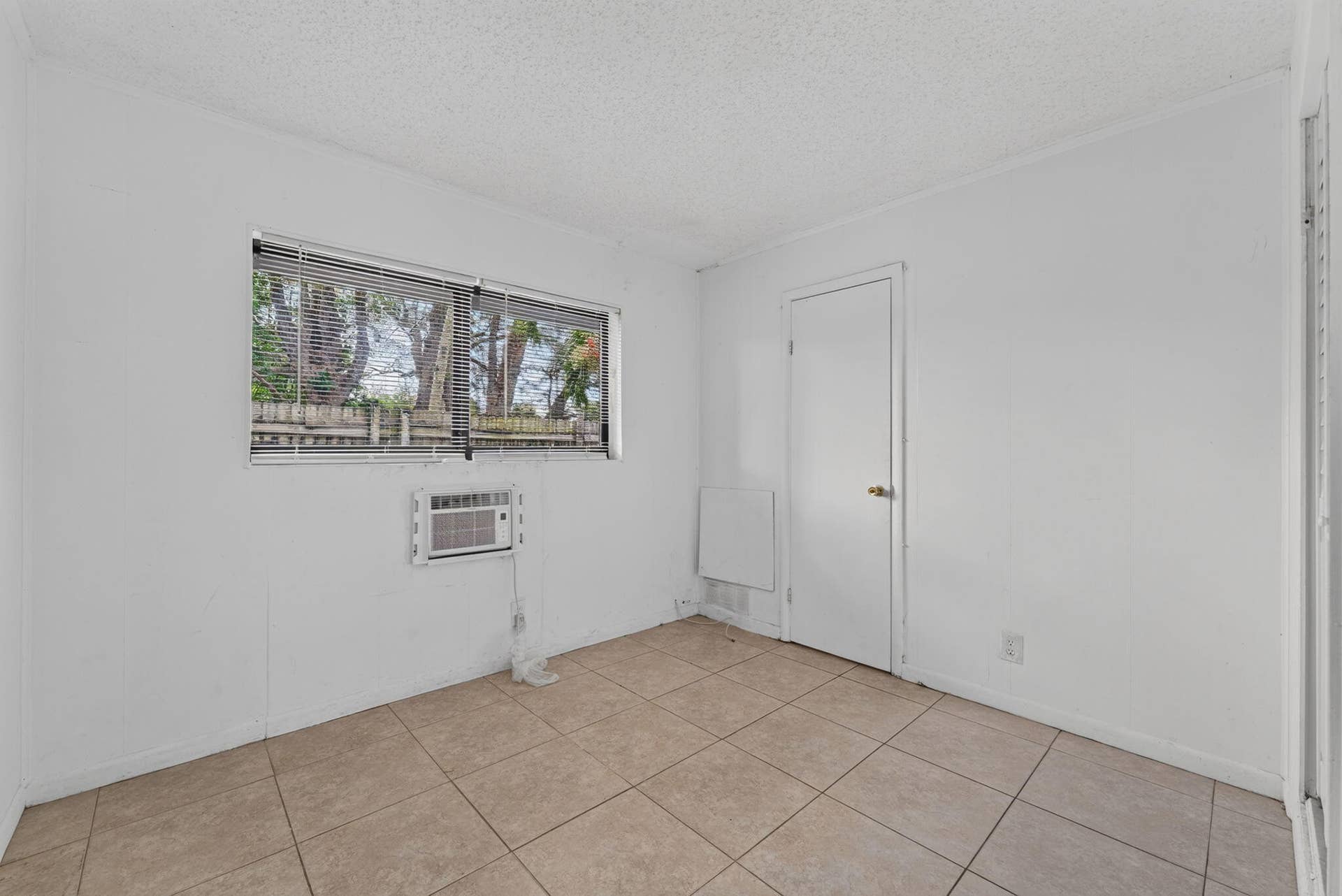 1224 NE 5TH Avenue, Fort Lauderdale, FL 33304 Room featuring neutral tile flooring, horizontal window blinds, and a built-in wall air conditioning unit