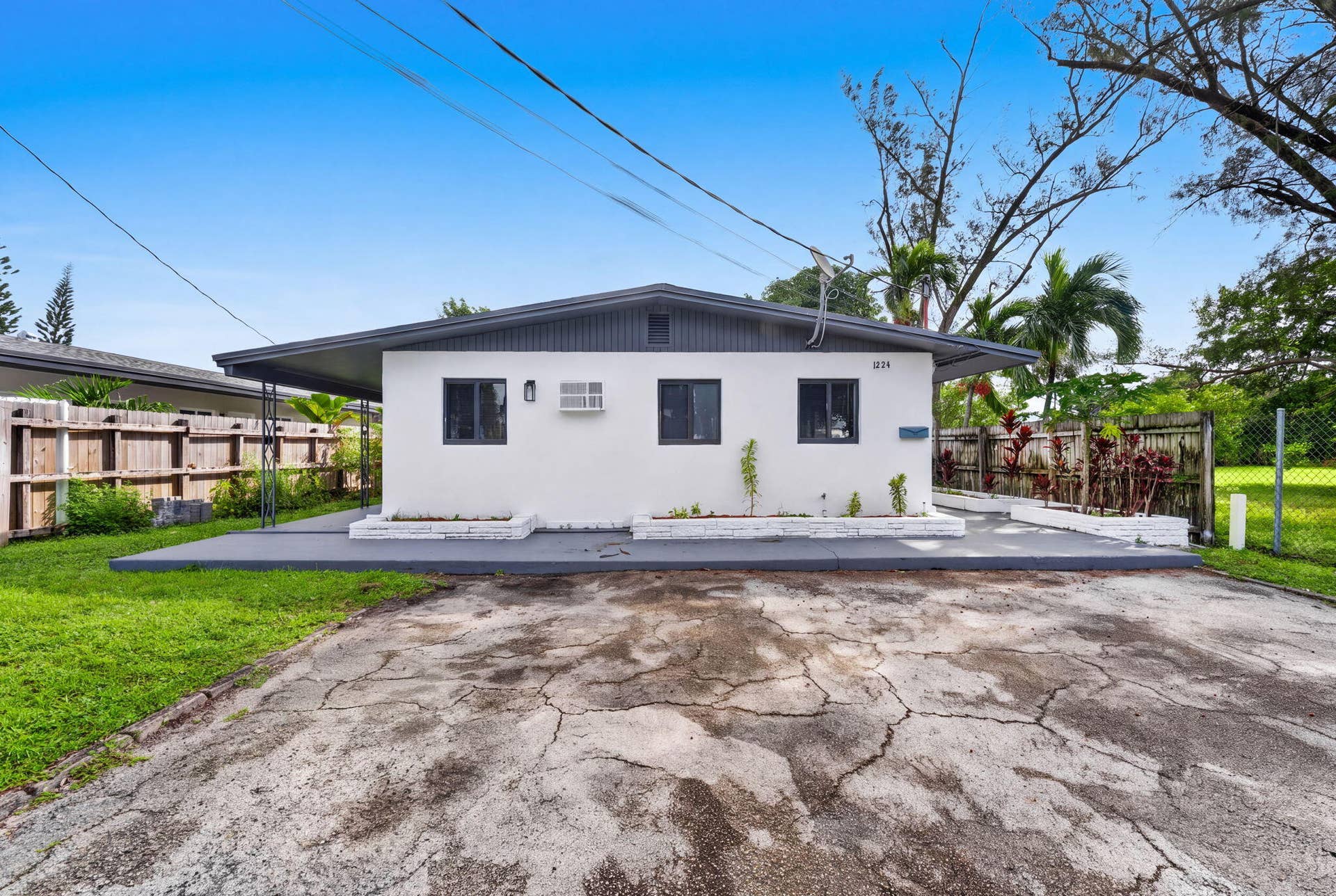 1224 NE 5TH Avenue, Fort Lauderdale, FL 33304 Single-story exterior featuring white stucco siding, a low-pitch roofline with dark trim, dual front-facing planters, and a concrete patio