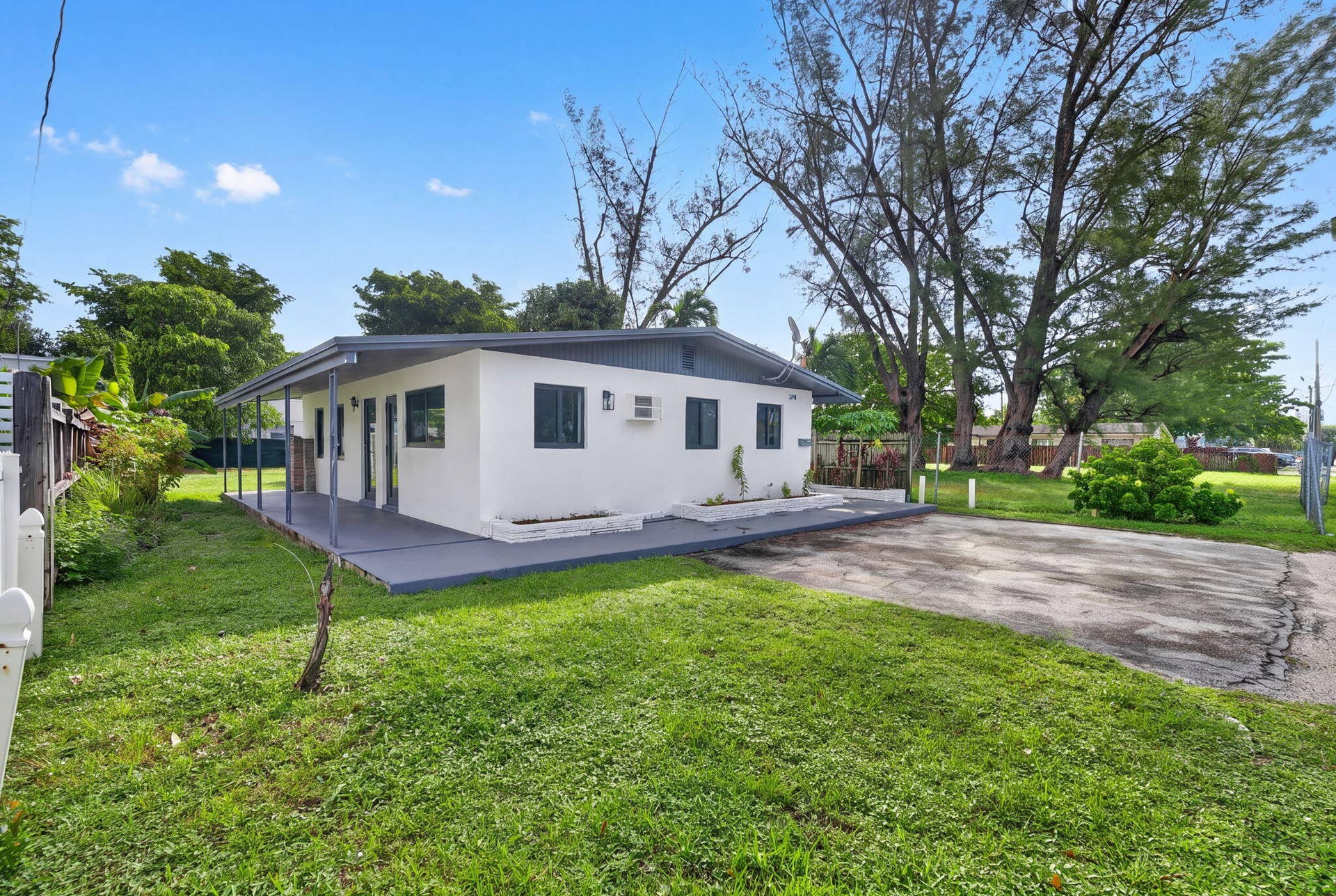1224 NE 5TH Avenue, Fort Lauderdale, FL 33304 Single-story residence featuring a covered patio, paved driveway, exterior stucco finish, and mature trees on the lot