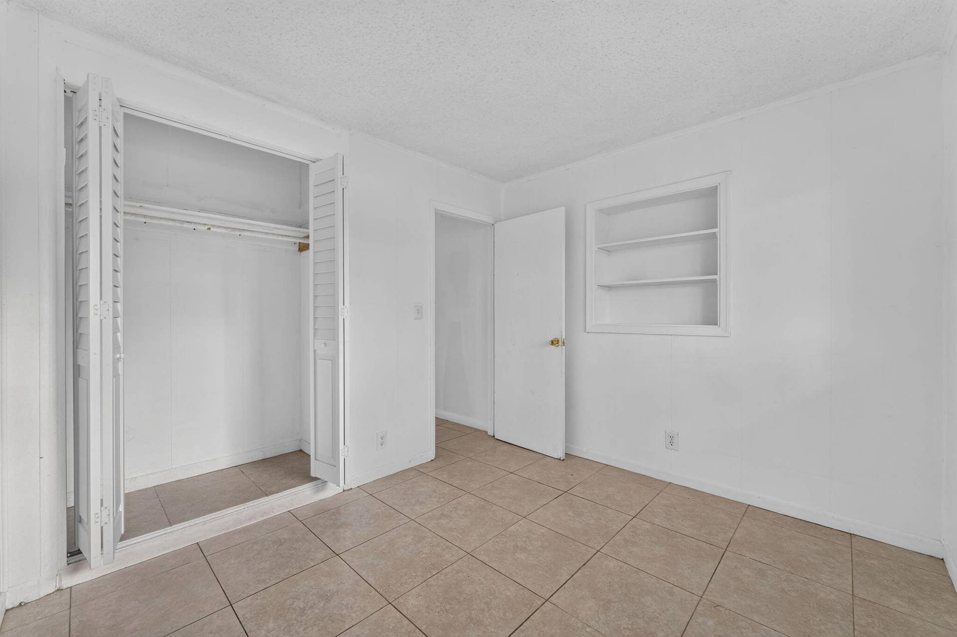 1224 NE 5TH Avenue, Fort Lauderdale, FL 33304 Interior space featuring neutral tile flooring, closet with bi-fold louvered doors, and built-in wall shelving
