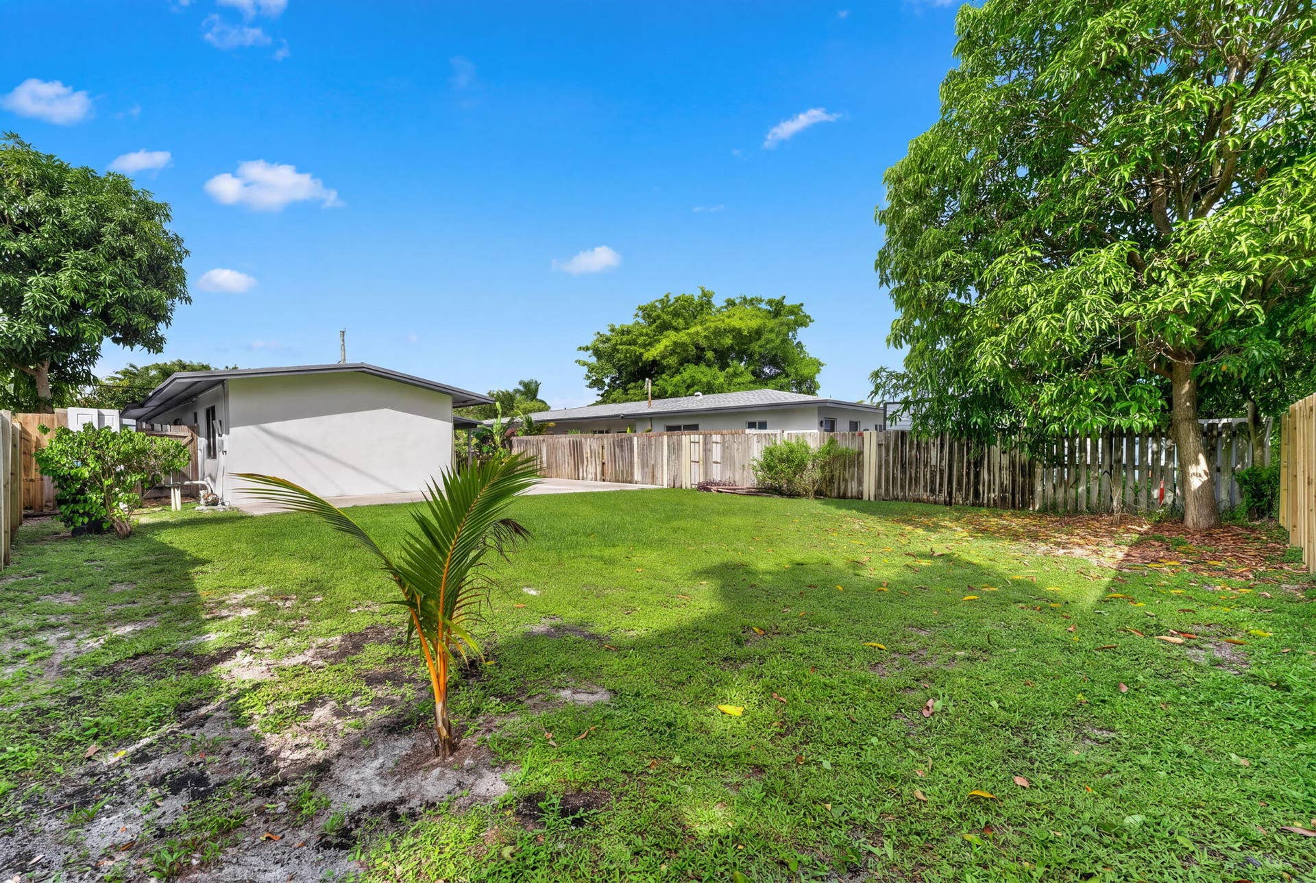 1224 NE 5TH Avenue, Fort Lauderdale, FL 33304 Expansive backyard featuring a sprawling lawn, mature trees, concrete patio, and a perimeter wood privacy fence