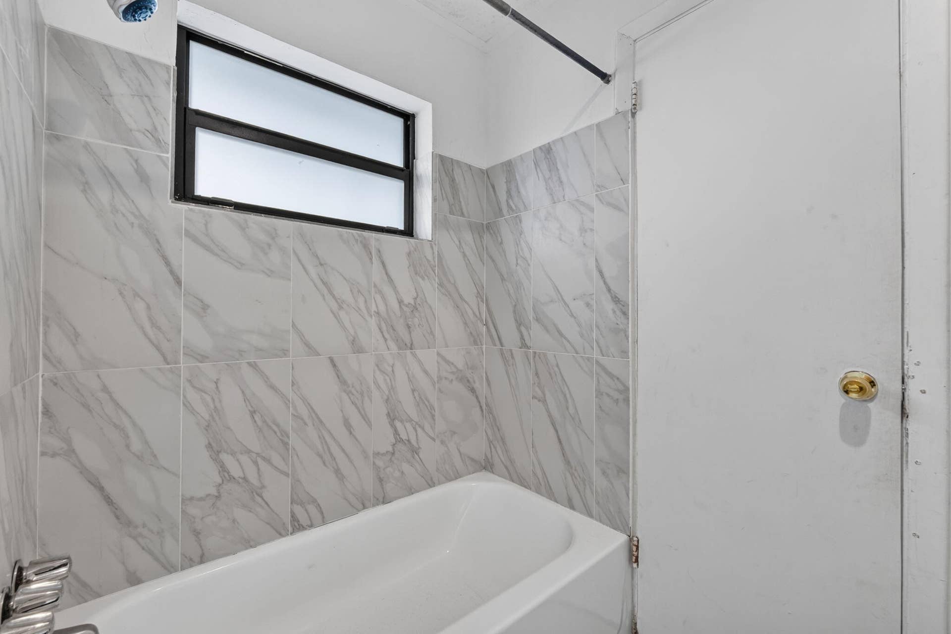 1224 NE 5TH Avenue, Fort Lauderdale, FL 33304 Bathtub featuring light-toned stone-patterned wall tile, integrated chrome hardware, and a single horizontal frosted-glass window