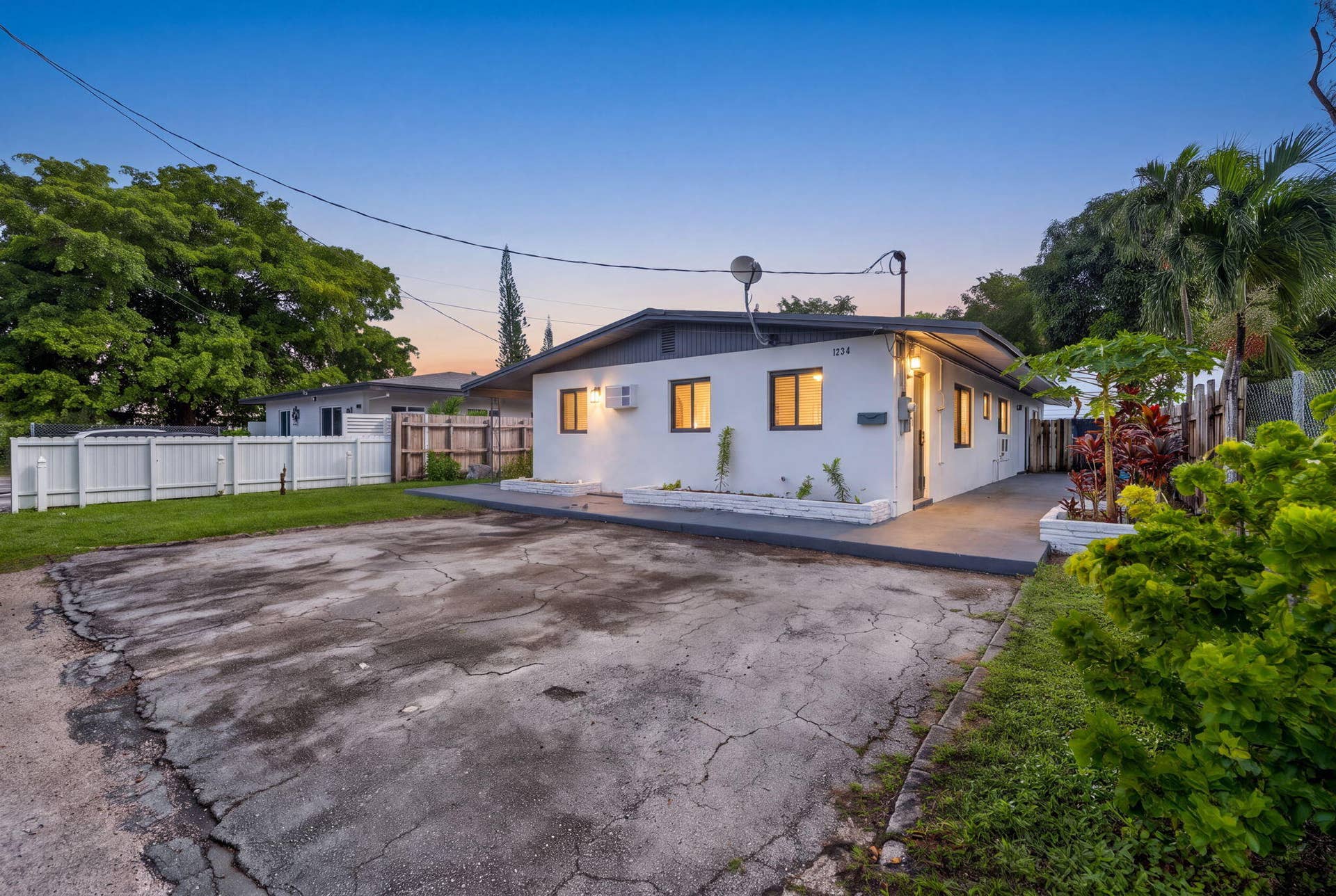 1224 NE 5TH Avenue, Fort Lauderdale, FL 33304 Single-story exterior featuring white stucco siding, a grey-toned roofline, paved driveway, and perimeter white vinyl fencing