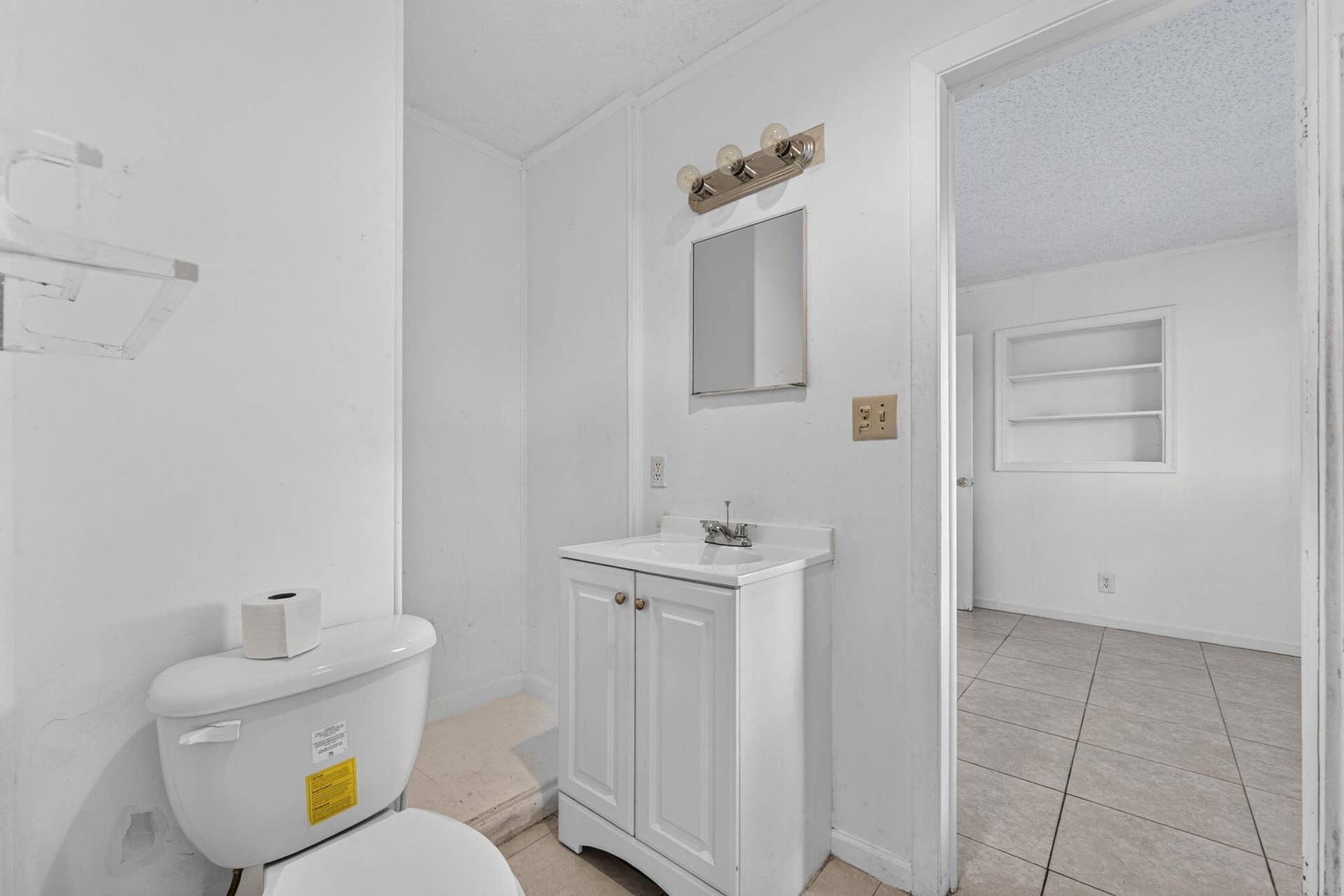 1224 NE 5TH Avenue, Fort Lauderdale, FL 33304 White vanity cabinet with an integrated sink and chrome faucet, wall-mounted light fixture, square mirror, and built-in wall shelving