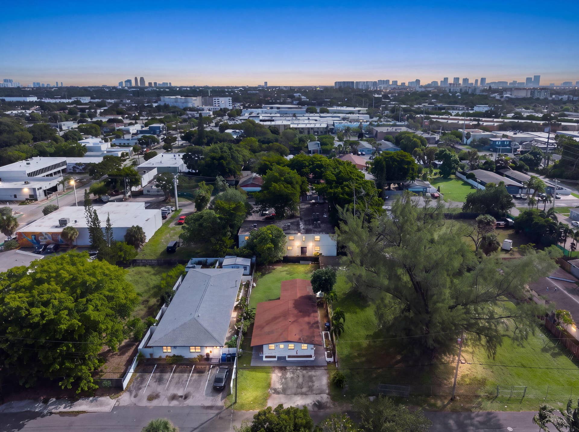 1224 NE 5TH Avenue, Fort Lauderdale, FL 33304 Aerial perspective of a property featuring expansive green space, mature canopy trees, paved off-street parking, and a distant city skyline