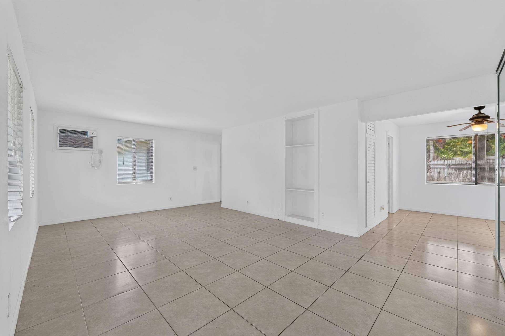 1224 NE 5TH Avenue, Fort Lauderdale, FL 33304 Neutral-toned tile flooring, built-in shelving, windows with blinds, ceiling fan with light fixture, and mounted wall air conditioning unit