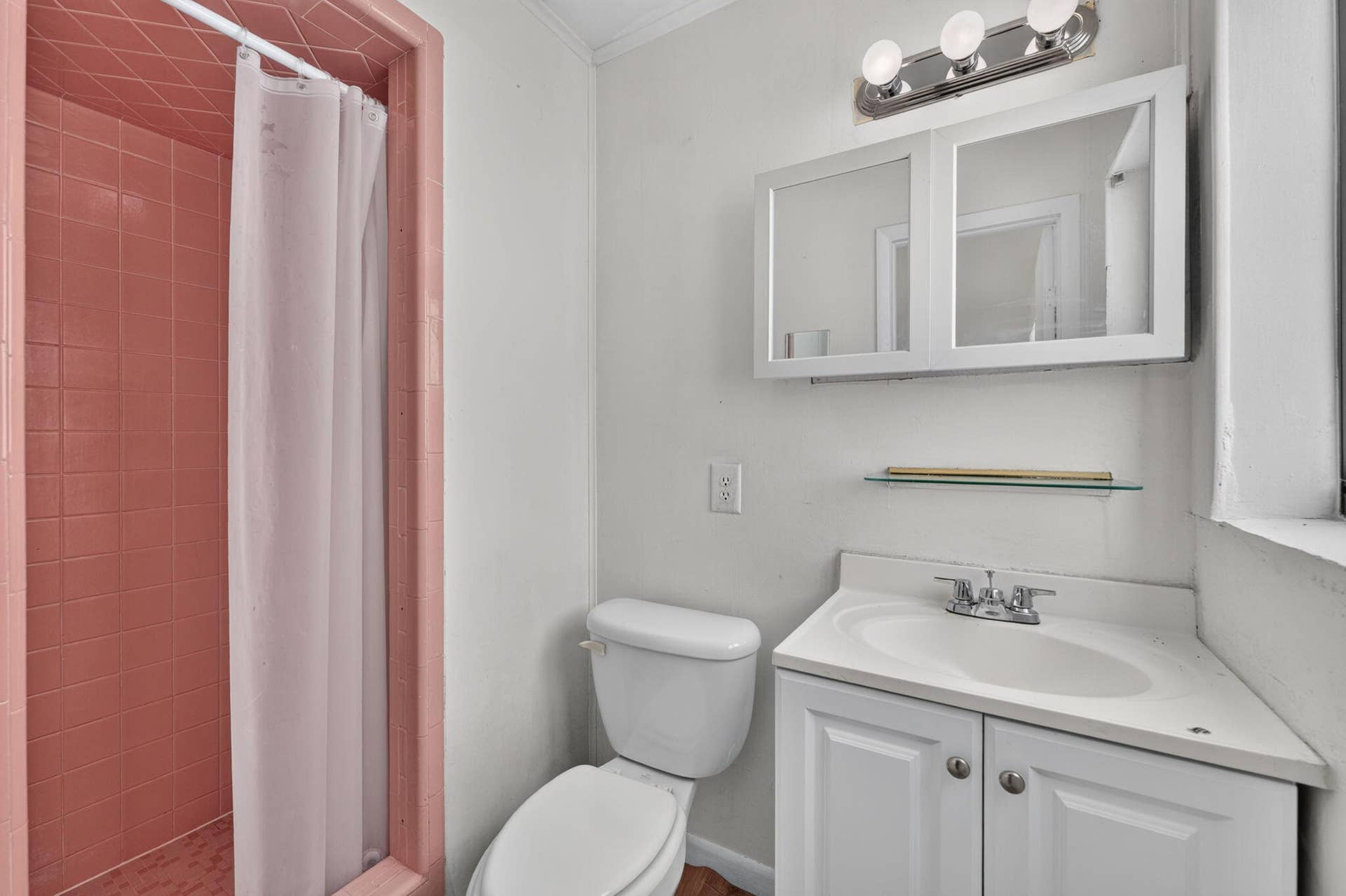 1224 NE 5TH Avenue, Fort Lauderdale, FL 33304 Bathroom featuring a shower stall with pink tile surround, white vanity cabinet with a integrated sink, double-door medicine cabinet, and three-bulb vanity light fixture