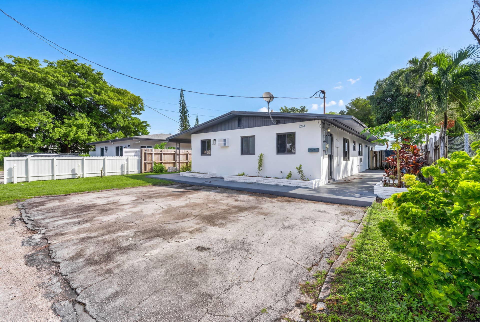 1224 NE 5TH Avenue, Fort Lauderdale, FL 33304 Single-story exterior featuring white stucco siding, a low-slope roof, paved driveway, and white vinyl perimeter fencing