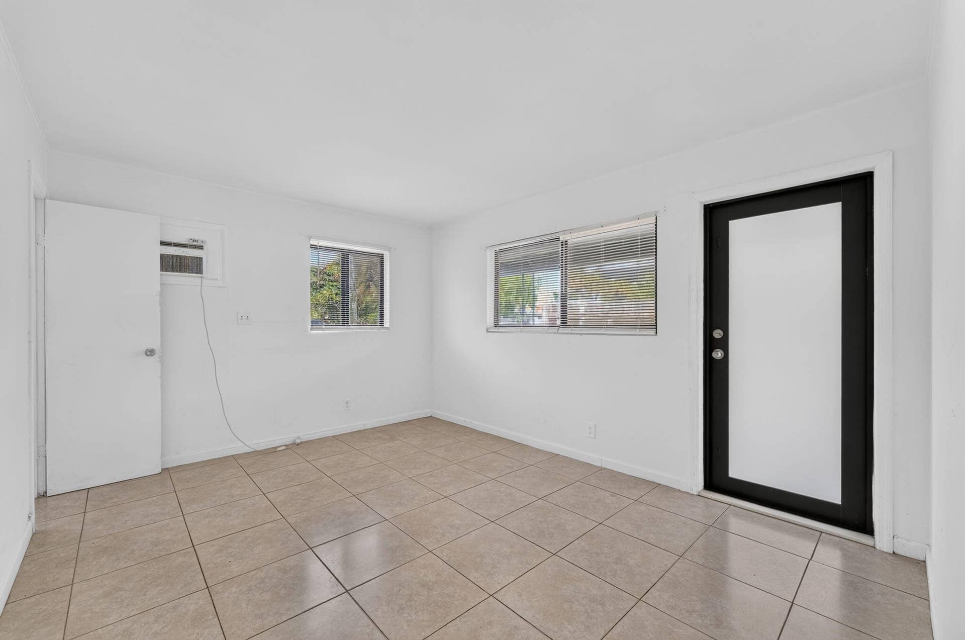 1224 NE 5TH Avenue, Fort Lauderdale, FL 33304 Interior space featuring neutral tile flooring, white wall finishes, dual-pane windows, and a black-framed exterior entry door