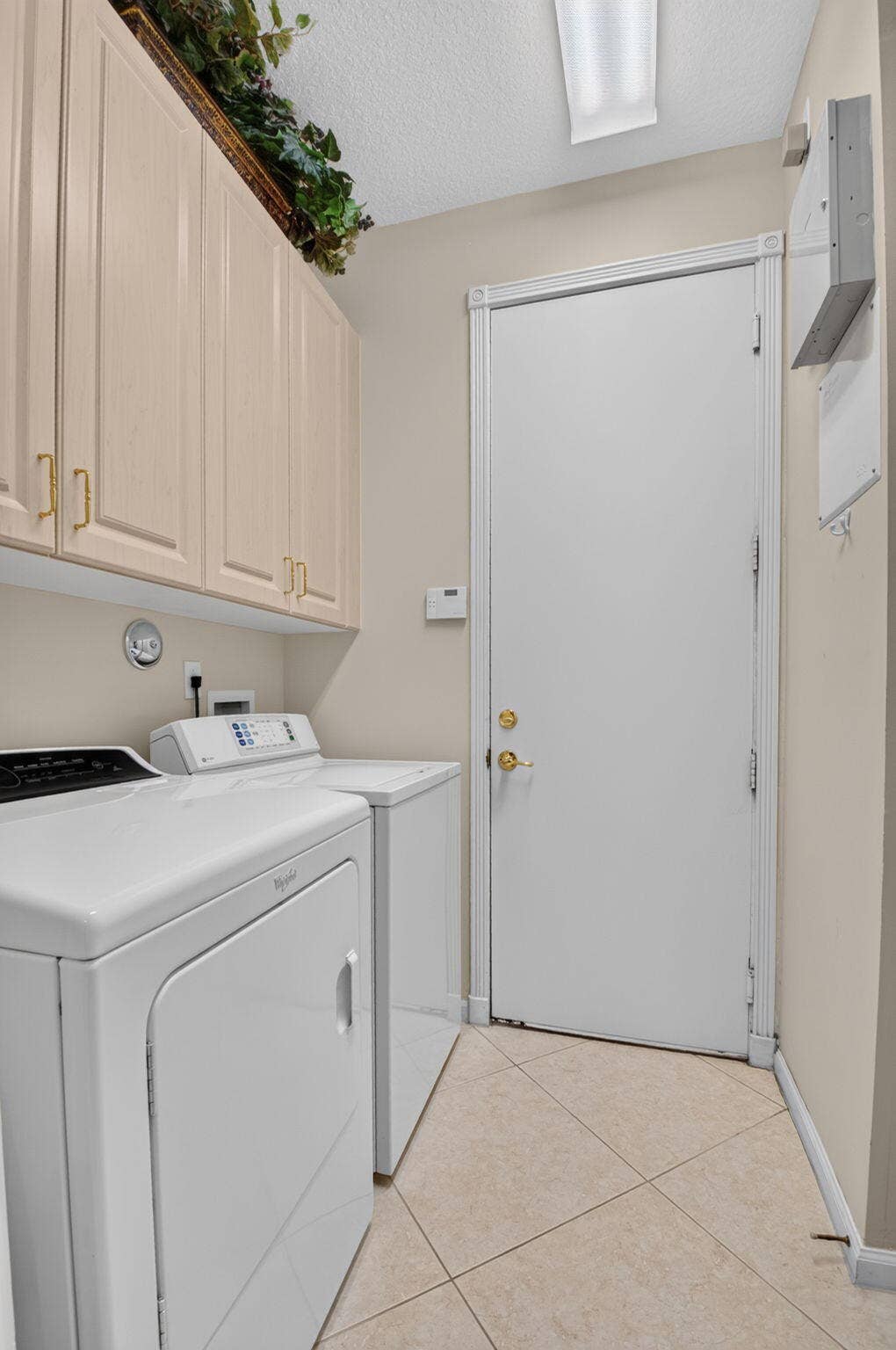 6874 Venidita Beach Drive, Delray Beach, FL 33446 Laundry area featuring light-toned cabinetry with brass-finish hardware, tile flooring, and a solid-panel door