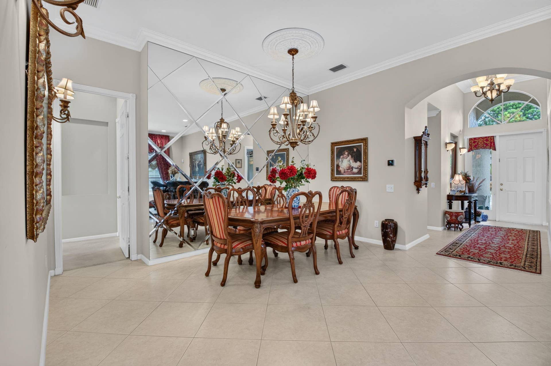 6874 Venidita Beach Drive, Delray Beach, FL 33446 Formal dining area featuring diamond-patterned wall mirrors, crown molding, arched entryways, tile flooring, and a decorative ceiling medallion with a multi-light chandelier