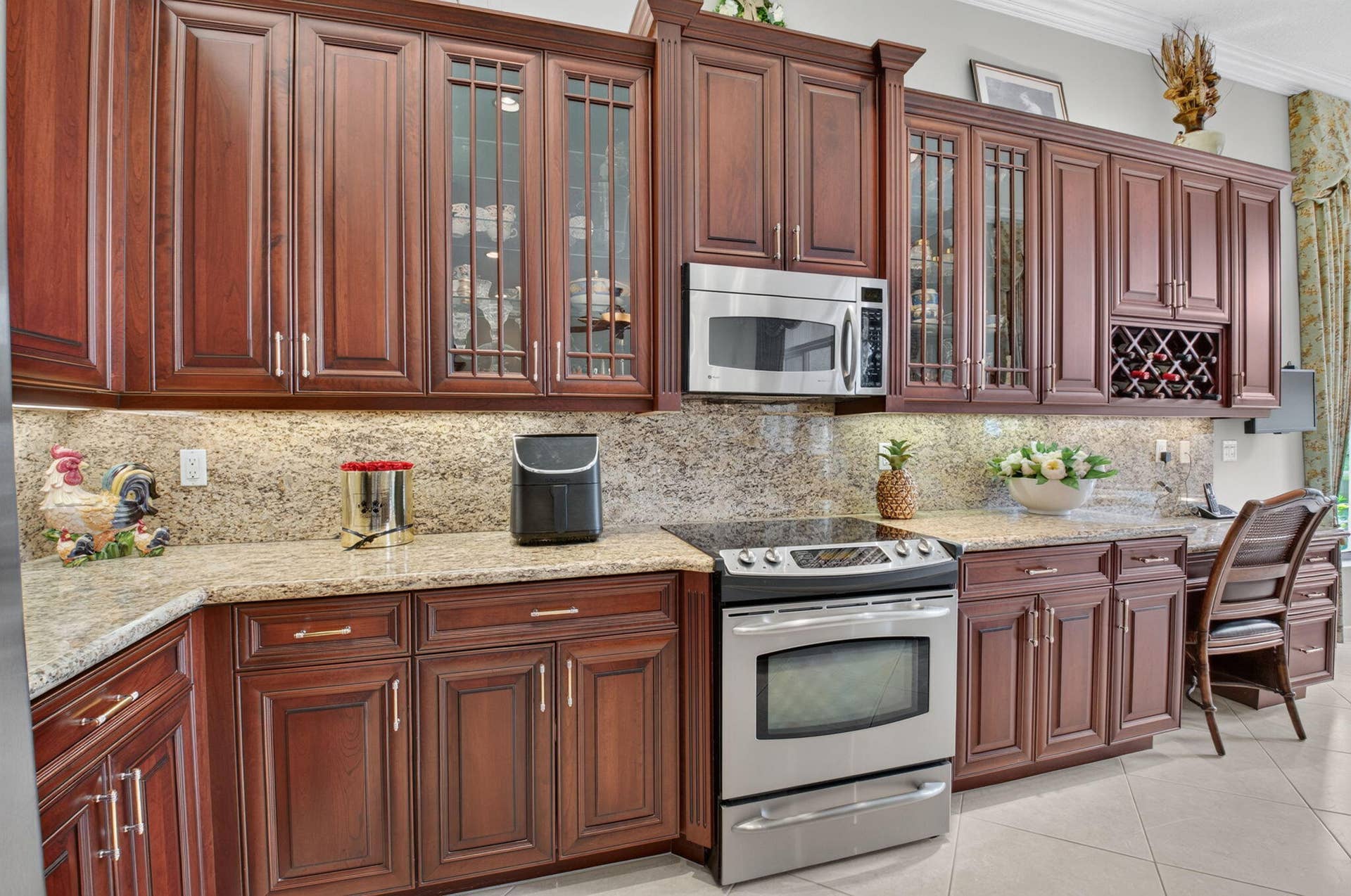 6874 Venidita Beach Drive, Delray Beach, FL 33446 Kitchen featuring rich-toned cabinetry with glass-paneled accents, stone countertops, stone tile backsplash, integrated wine storage, and stainless steel appliances