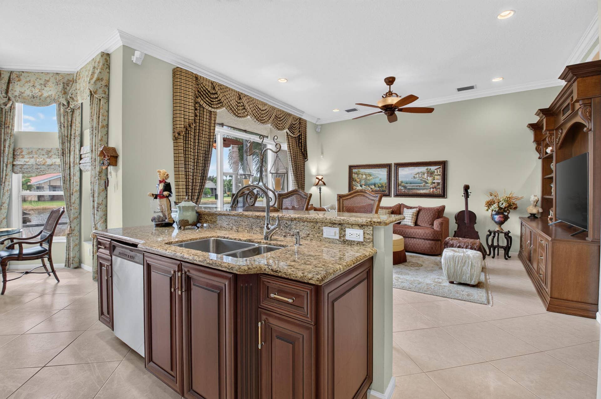 6874 Venidita Beach Drive, Delray Beach, FL 33446 Kitchen featuring dark wood cabinetry, stone-surface countertops, a dual-basin stainless steel sink, large-format tile flooring, and a built-in wood entertainment console