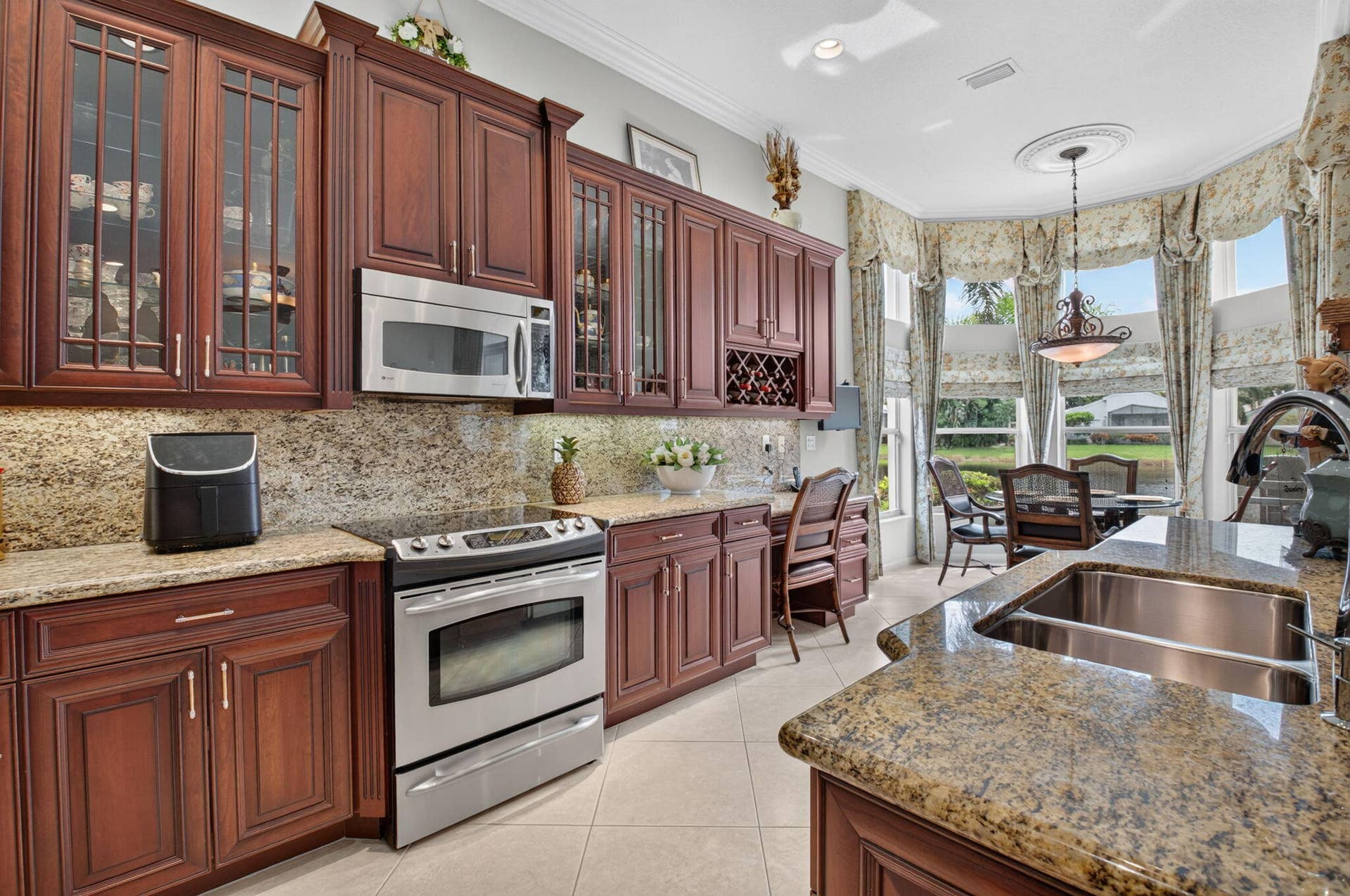 6874 Venidita Beach Drive, Delray Beach, FL 33446 Kitchen featuring raised-panel cherry wood cabinetry, stone countertops, integrated wine rack, stainless steel appliance suite, and a multi-paneled bay window with crown molding