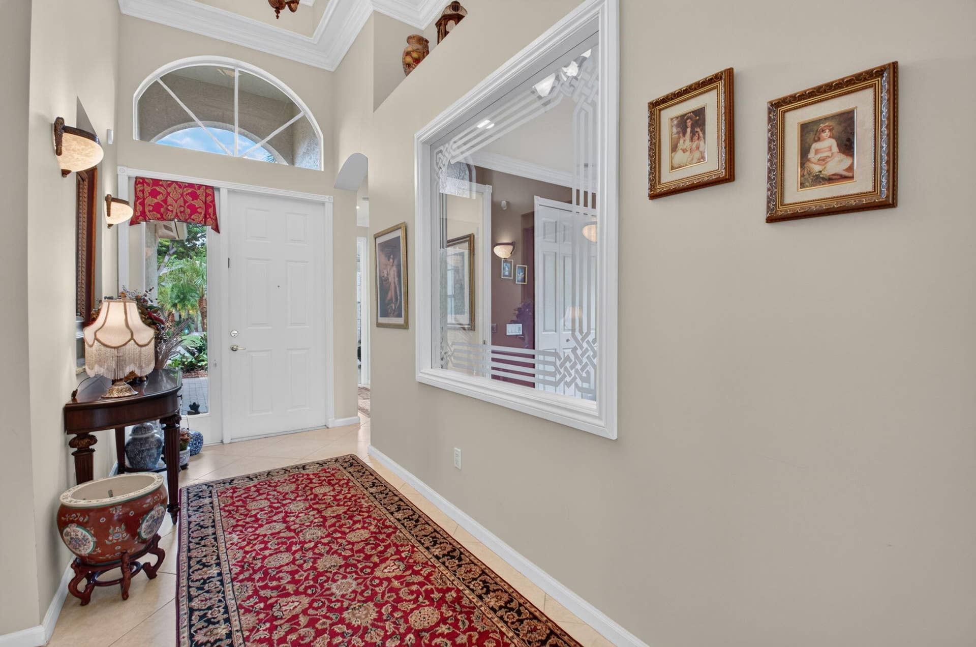 6874 Venidita Beach Drive, Delray Beach, FL 33446 Entryway featuring a high ceiling with crown molding, an arched transom window, ceramic tile flooring, wall-mounted light fixtures, and a decorative interior glass panel