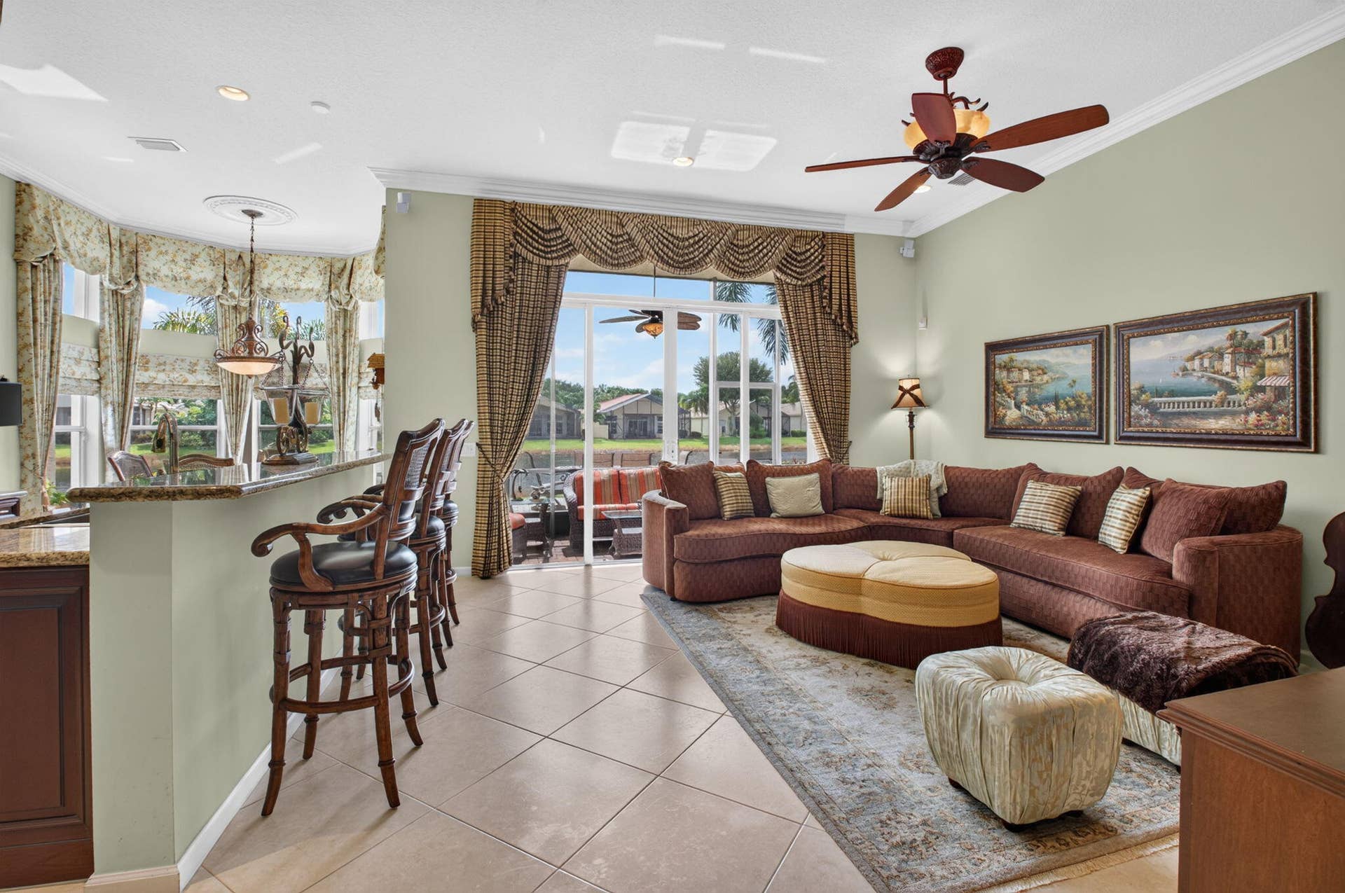 6874 Venidita Beach Drive, Delray Beach, FL 33446 Open-concept area featuring stone-surfaced breakfast bar, large-format tile flooring, crown molding, ceiling fan with integrated lighting, and expansive glass sliding doors