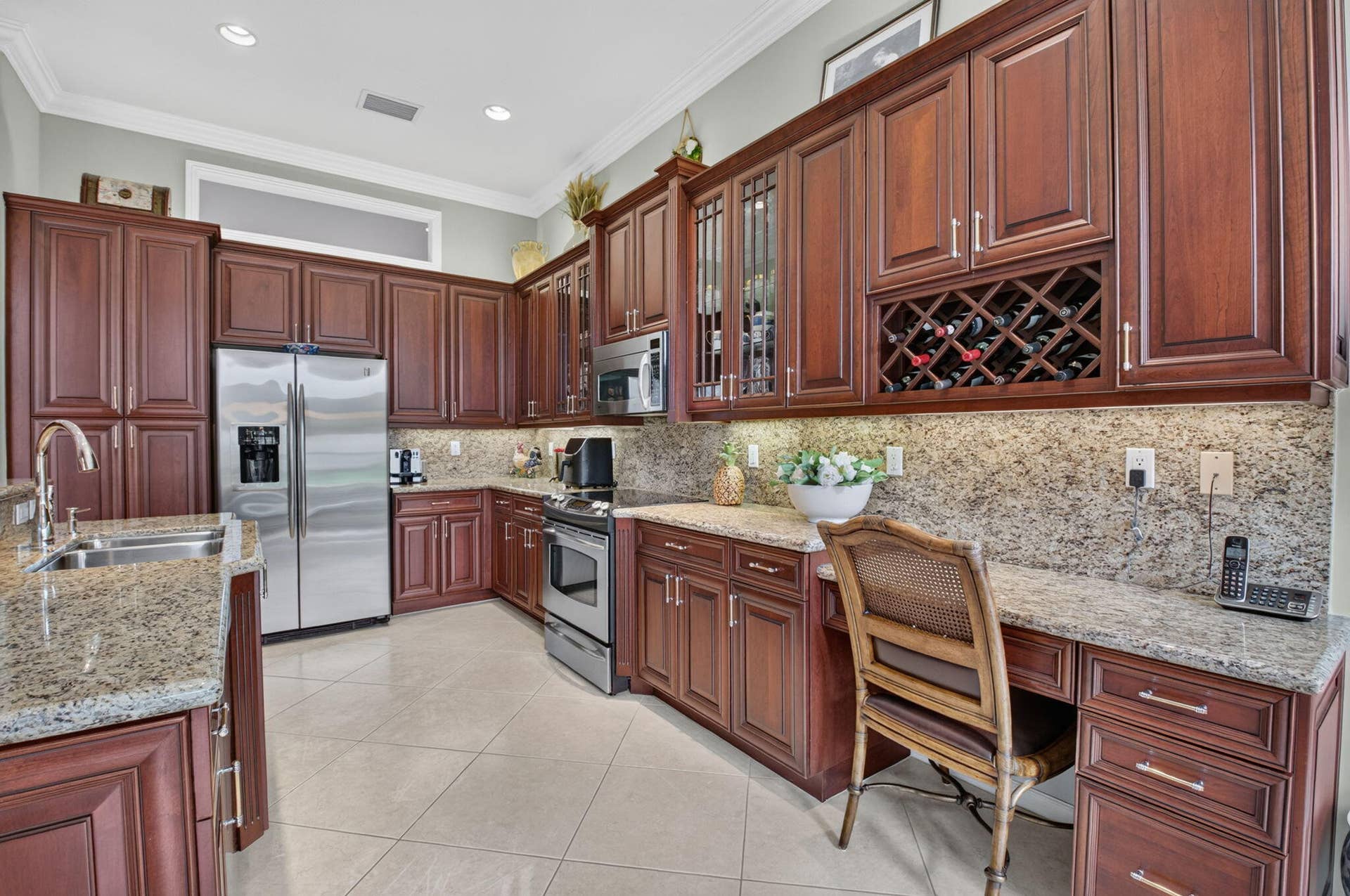 6874 Venidita Beach Drive, Delray Beach, FL 33446 Kitchen featuring cherry-tone cabinetry, stone countertops, stainless steel appliances, a built-in wine rack, and a dedicated desk workspace