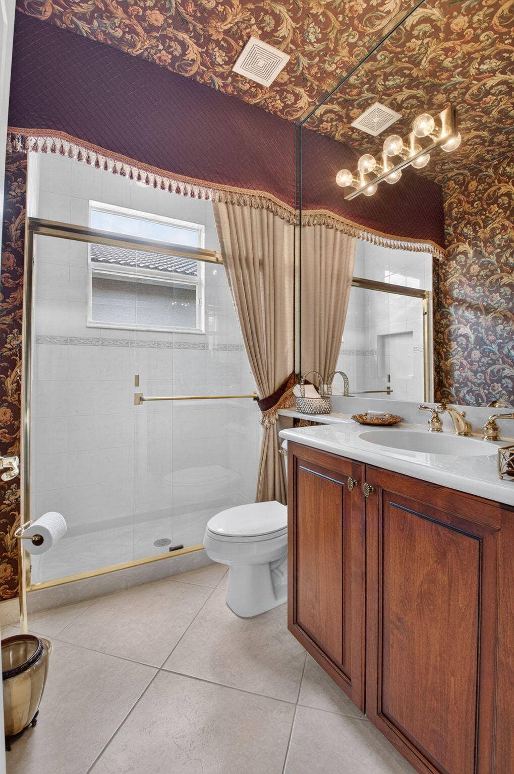 6874 Venidita Beach Drive, Delray Beach, FL 33446 Bathroom featuring wood-finish vanity cabinetry, a rectangular white countertop with an integrated sink, glass-enclosed shower with gold-tone hardware, and large-format tile flooring