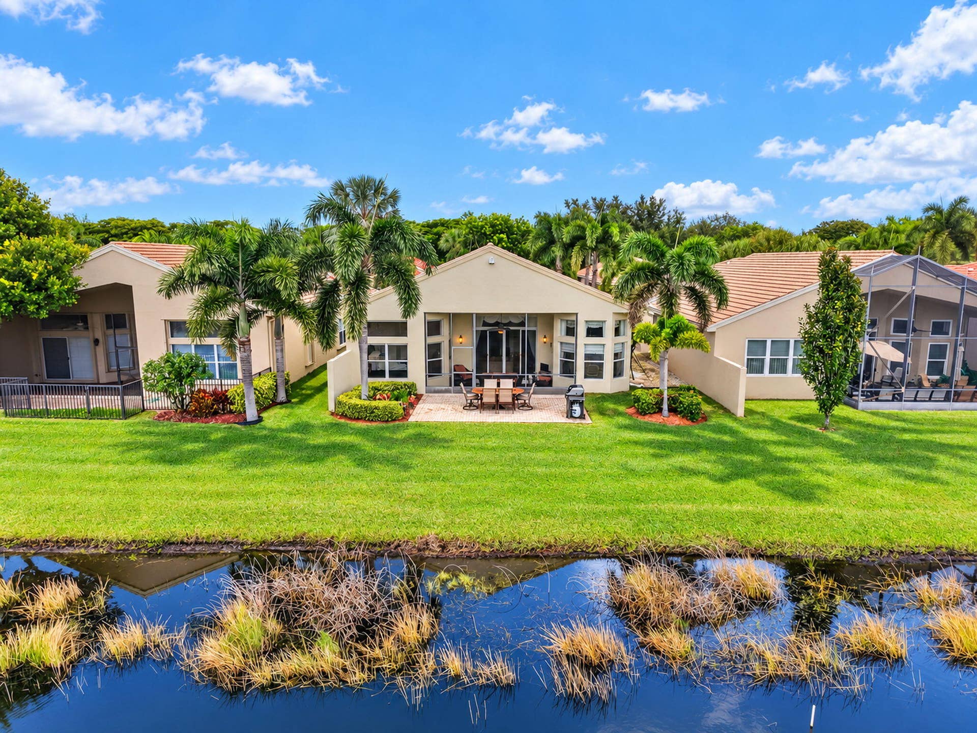 6874 Venidita Beach Drive, Delray Beach, FL 33446 Waterfront property featuring a concrete paver patio, stucco exterior, tile roofing, and mature palm trees