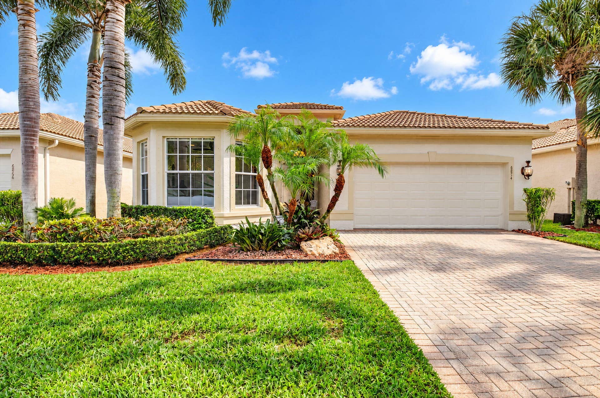 6874 Venidita Beach Drive, Delray Beach, FL 33446 Stucco exterior featuring a tile roof, bay window, paved driveway, and curated tropical landscaping